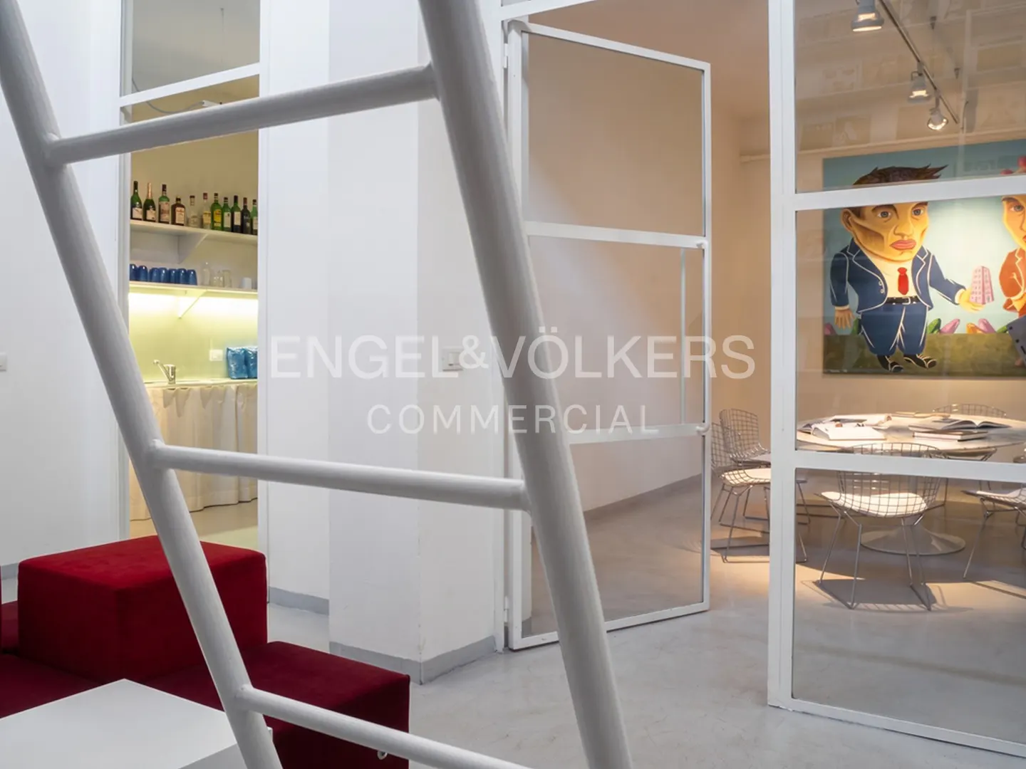 Interior view of a modern office space with white walls, red seating, and glass-enclosed meeting room with a round table and chairs.