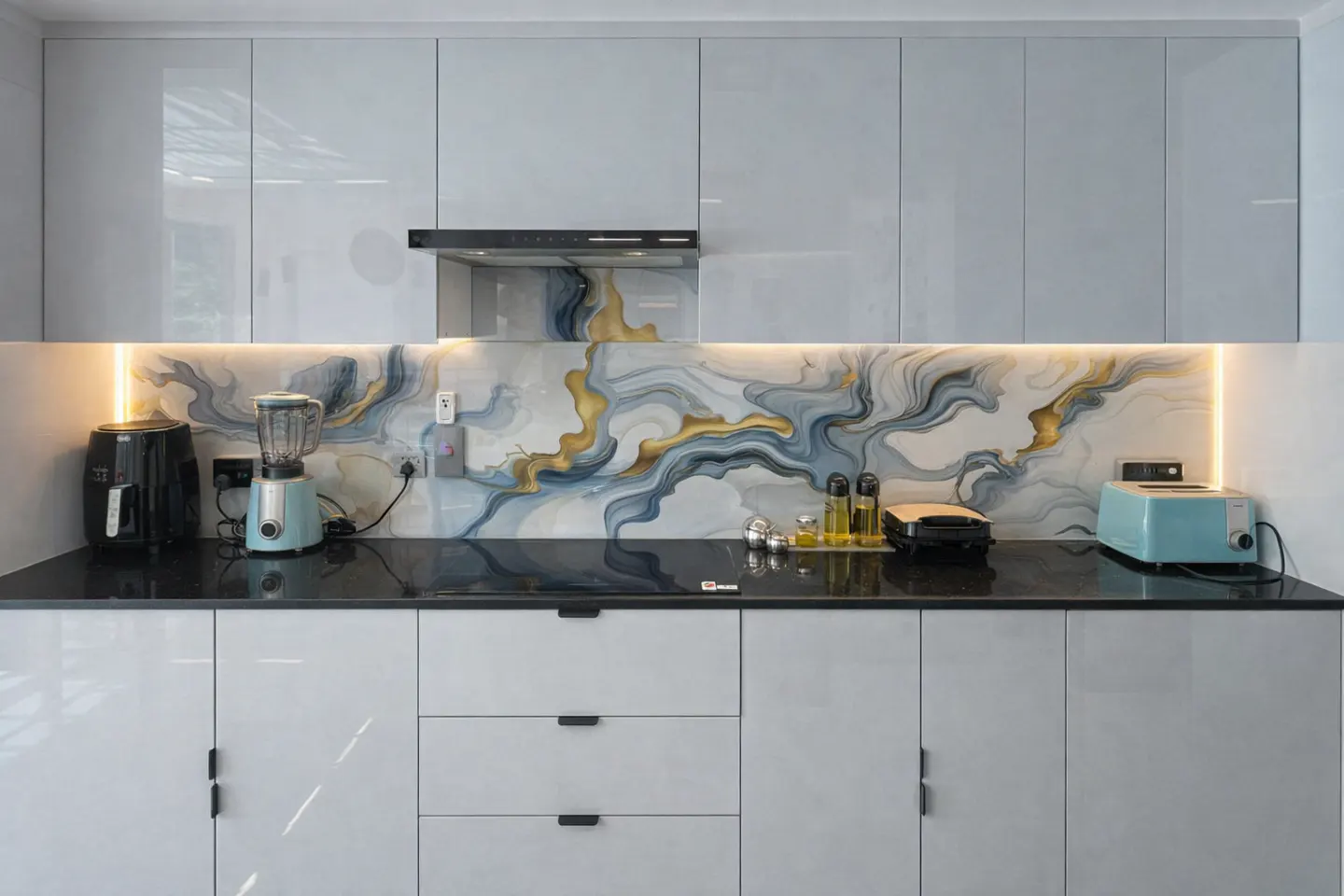 Modern kitchen with gray cabinets, black countertop, and marble-patterned backsplash with gold and blue accents. Appliances include a blender and toaster.