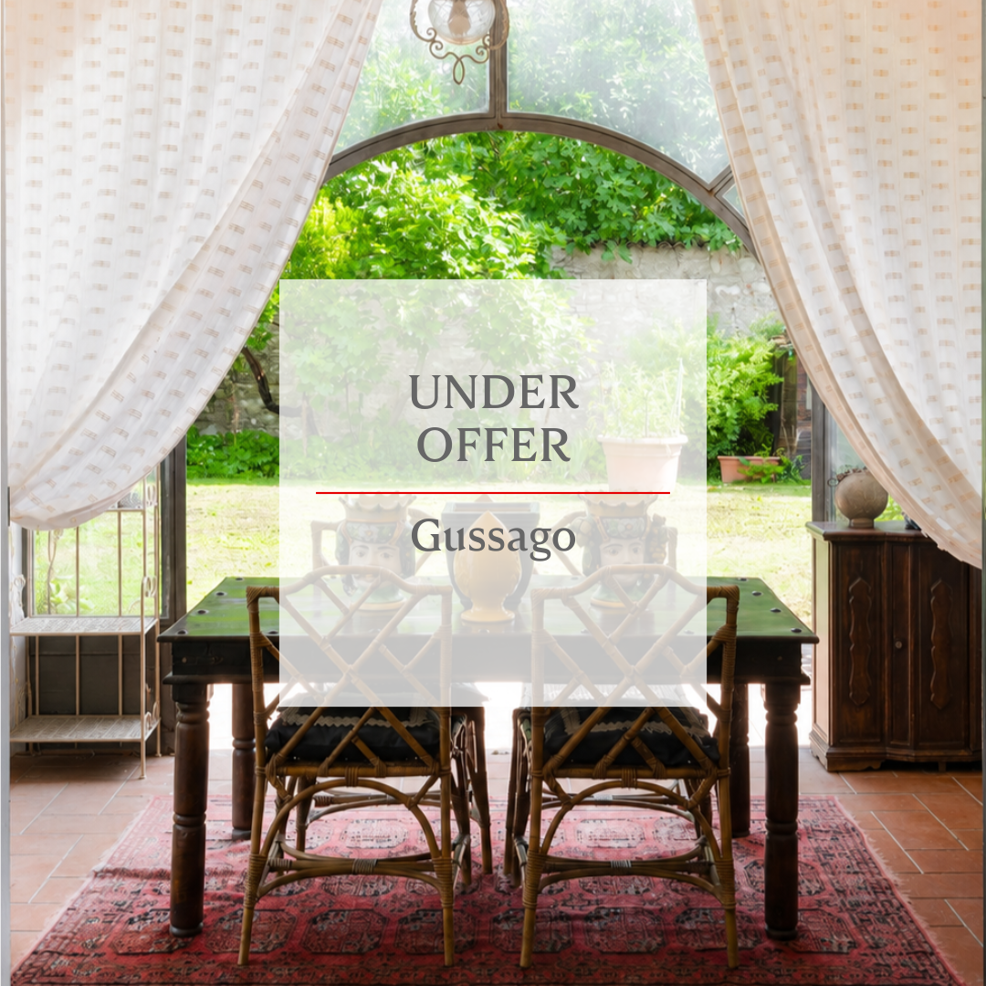 Dining room with bamboo chairs, dark wood table, and red rug, overlooking a garden through large arched windows. [AI-generated text]