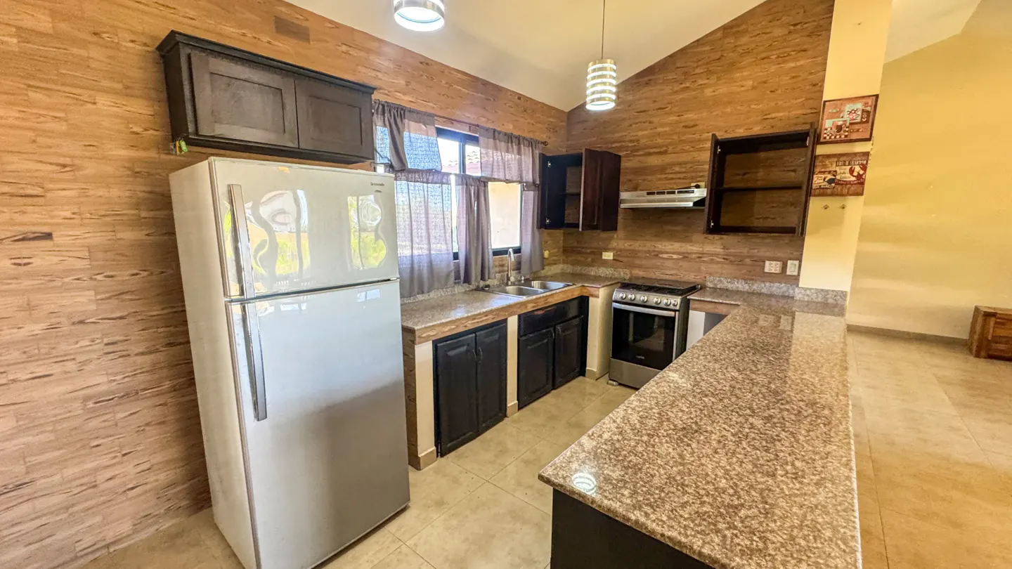 A kitchen with wood-look walls, dark cabinets, granite countertops, and a stainless steel oven. A white refrigerator is on the left.