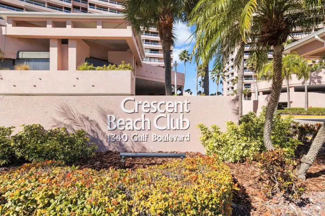 Exterior shot of Crescent Beach Club sign with palm trees and building in the background.