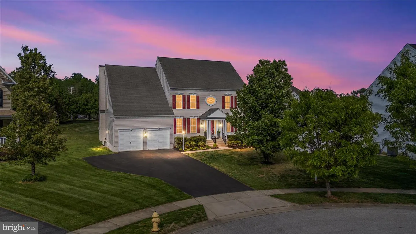 Two-story beige house with red shutters, a black roof, and a two-car garage at dusk.