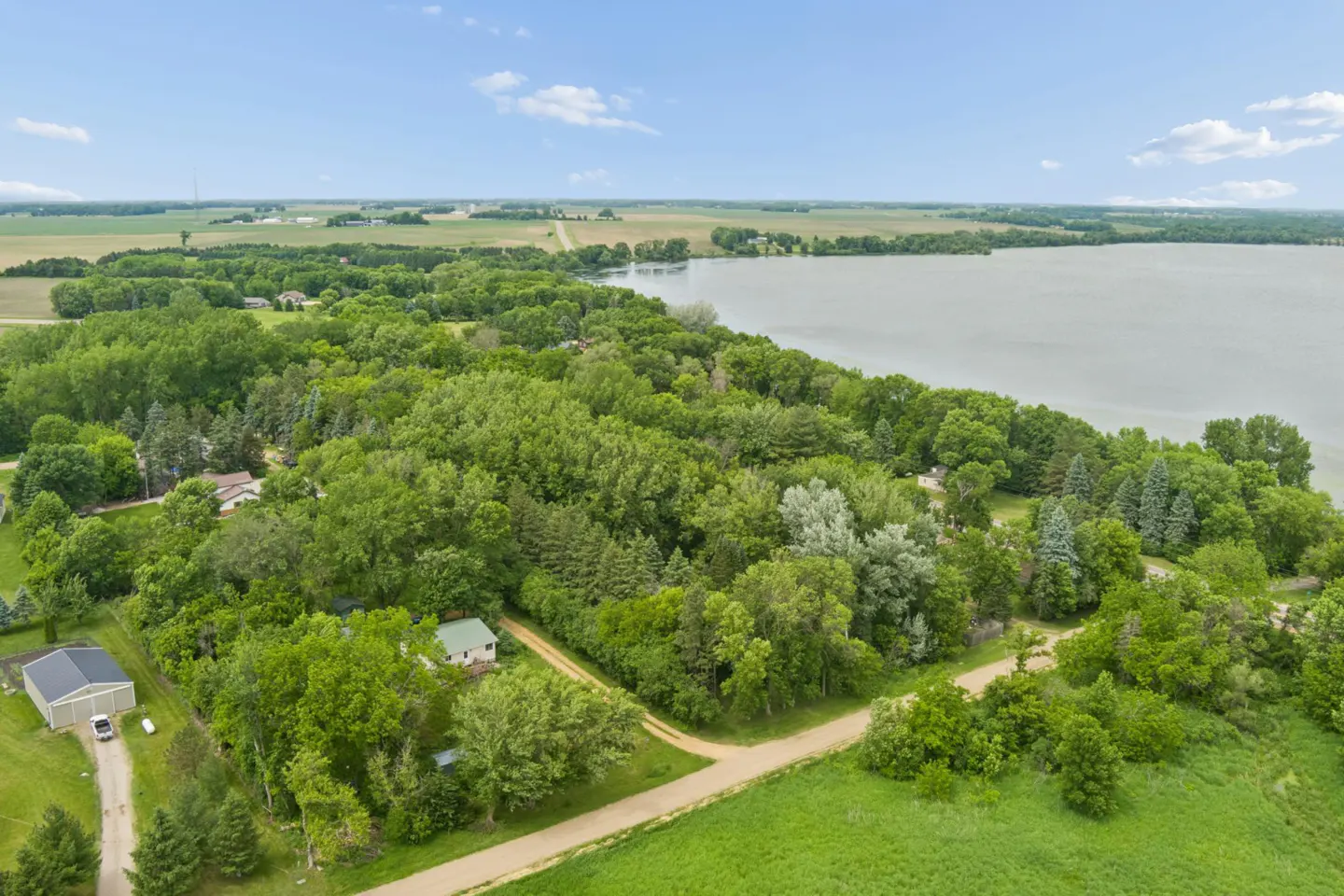 Aerial view of a wooded property with a house and garage, situated next to a large lake and open farmland.