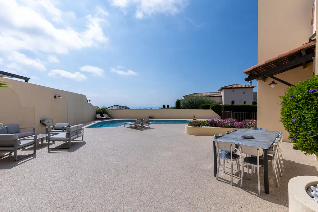 Outdoor patio with a pool, lounge chairs, and dining table under a blue sky.