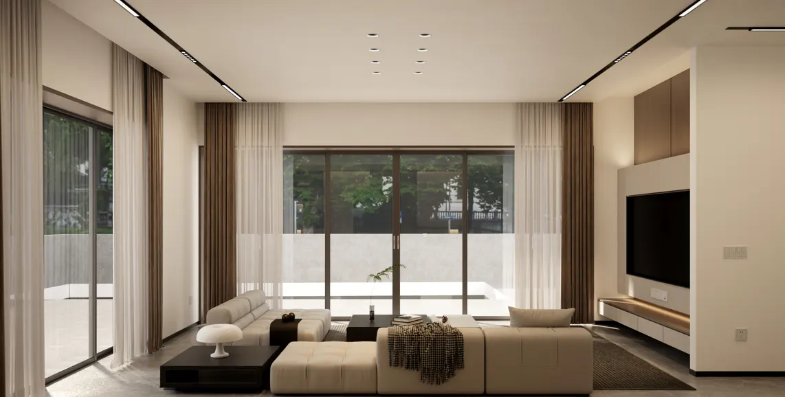 A bright living room with beige sofas, dark wood tables, and a large window with sheer white curtains. A TV is mounted on the wall.