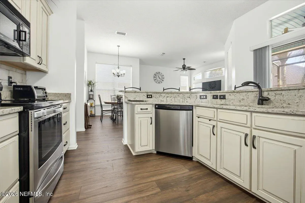 Modern kitchen with white cabinets, granite countertops, stainless steel appliances, and wood-look floors, open to dining.