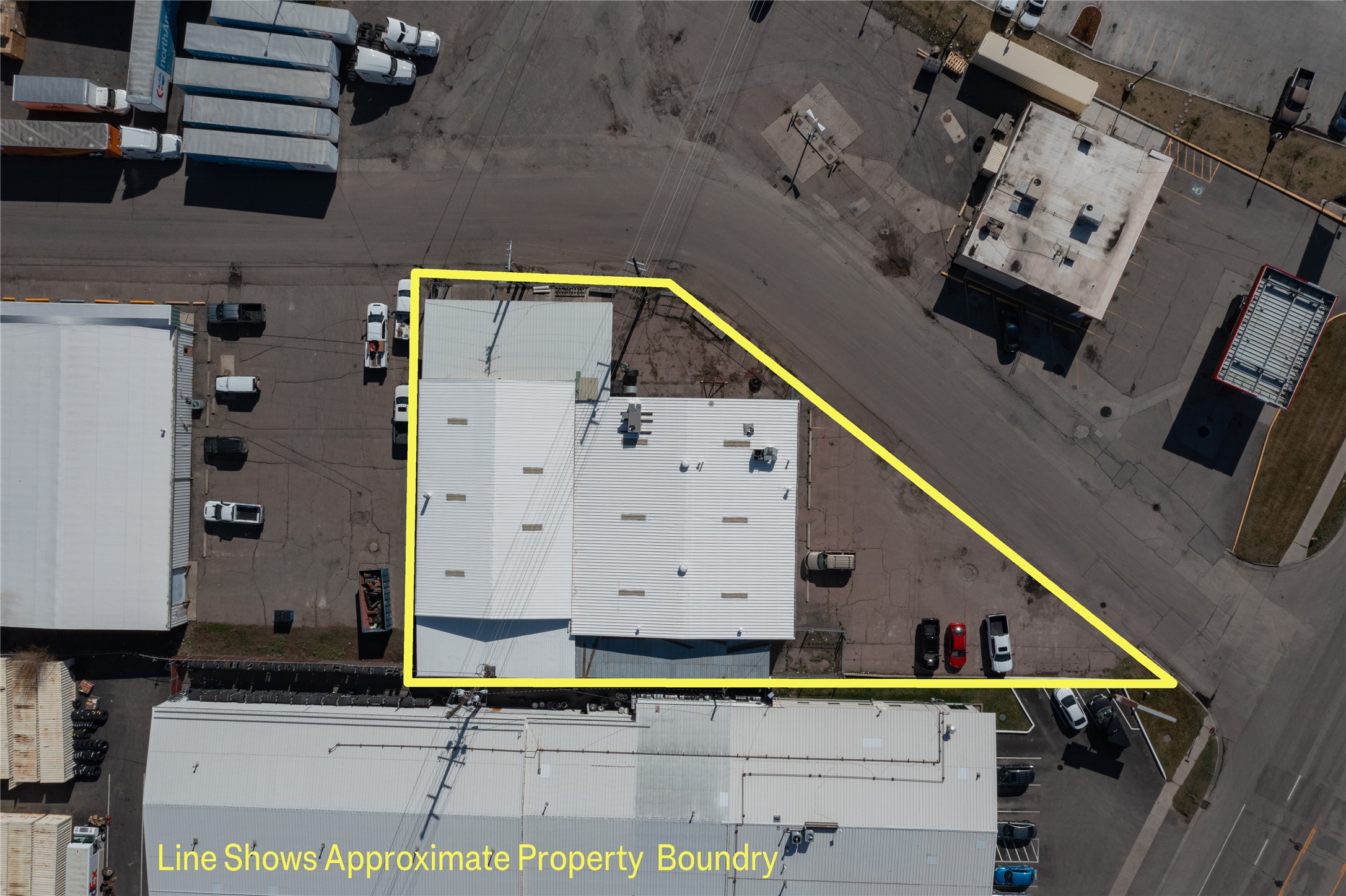 Aerial view of a commercial property with a yellow line indicating the boundary. The building has a white roof and is surrounded by parking lots and roads.
