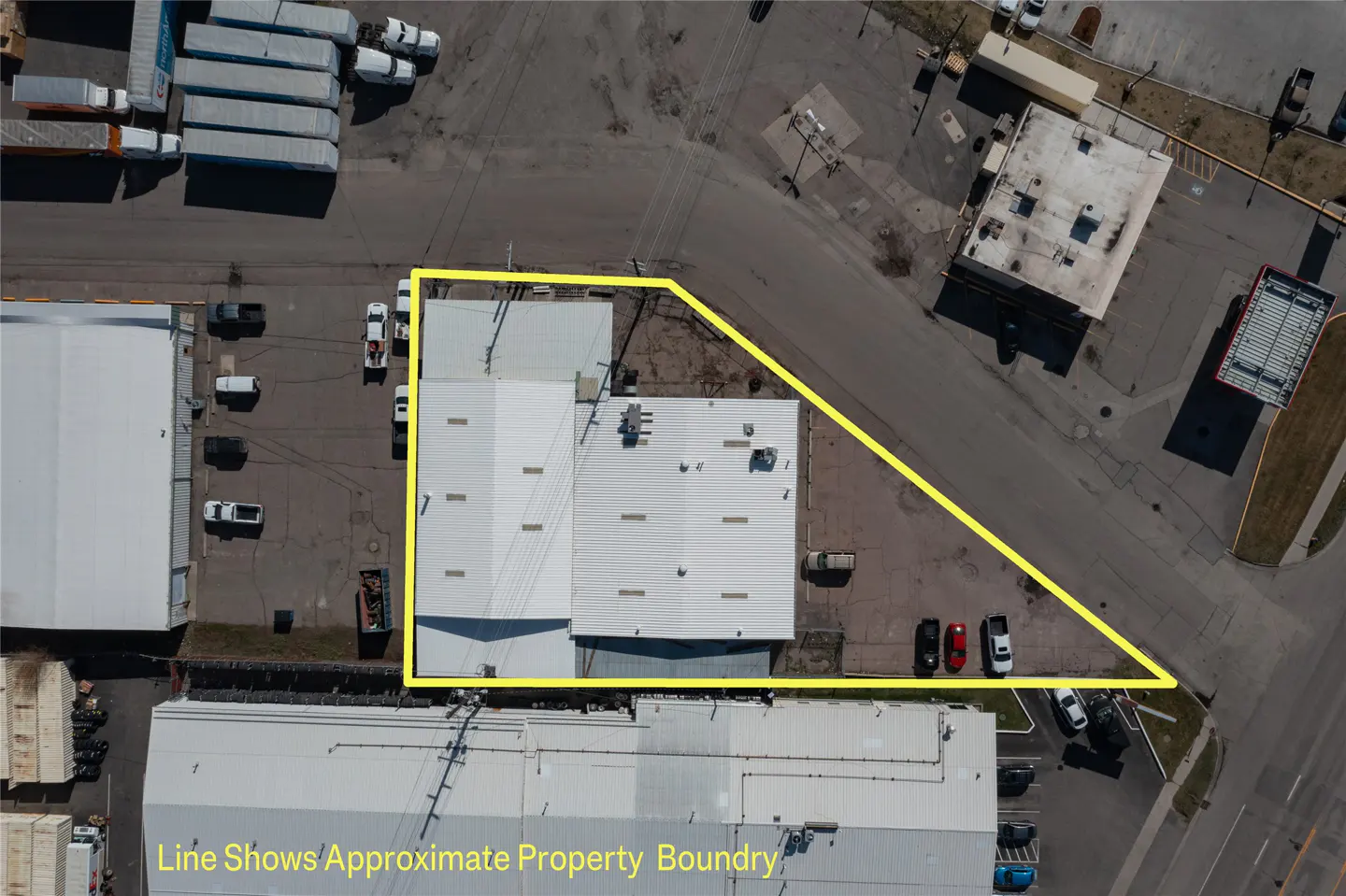 Aerial view of a commercial property with a yellow line indicating the boundary. The building has a white roof and is surrounded by parking lots and roads.