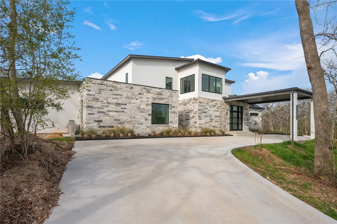 Modern two-story home with stone and white siding, black framed windows, and a concrete driveway under a blue sky.