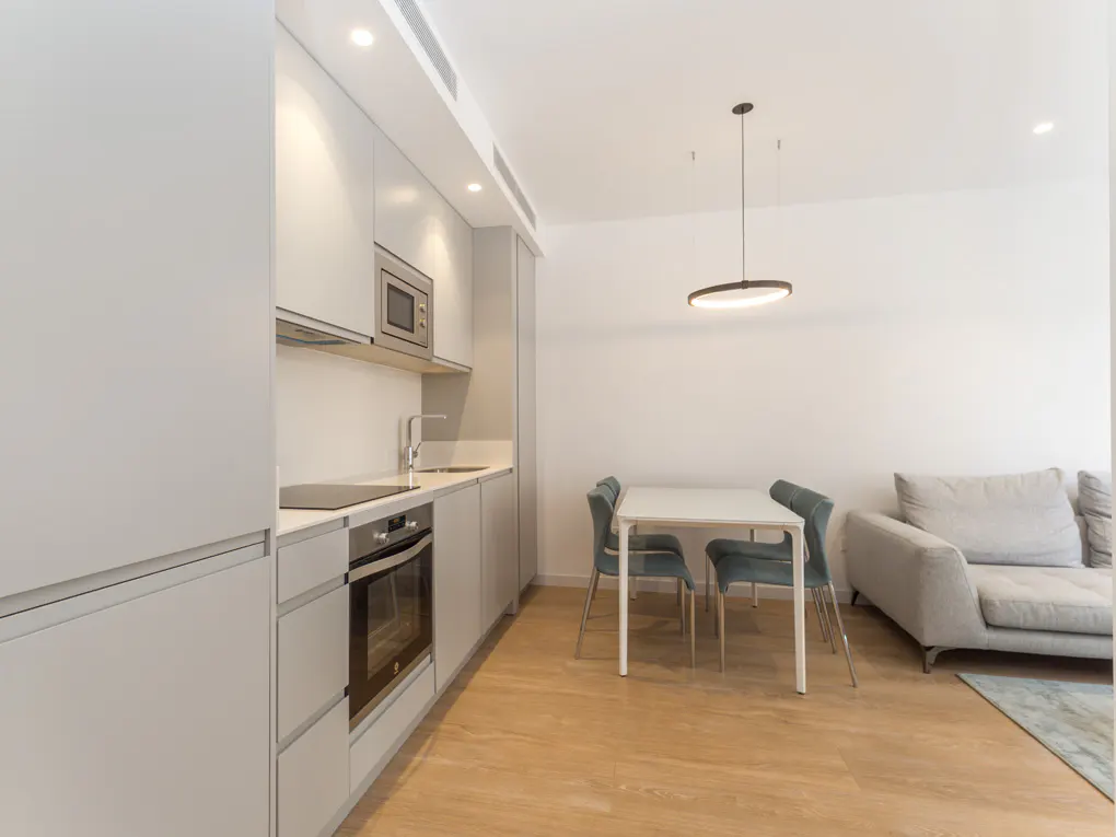 A modern apartment interior with gray cabinets, a white dining table with blue chairs, and a gray sofa.