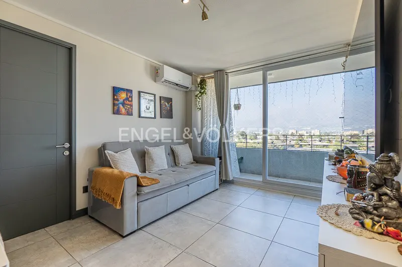 Living room with a gray sofa, pillows, and a yellow blanket. Balcony with city view. Three framed pictures on the wall.