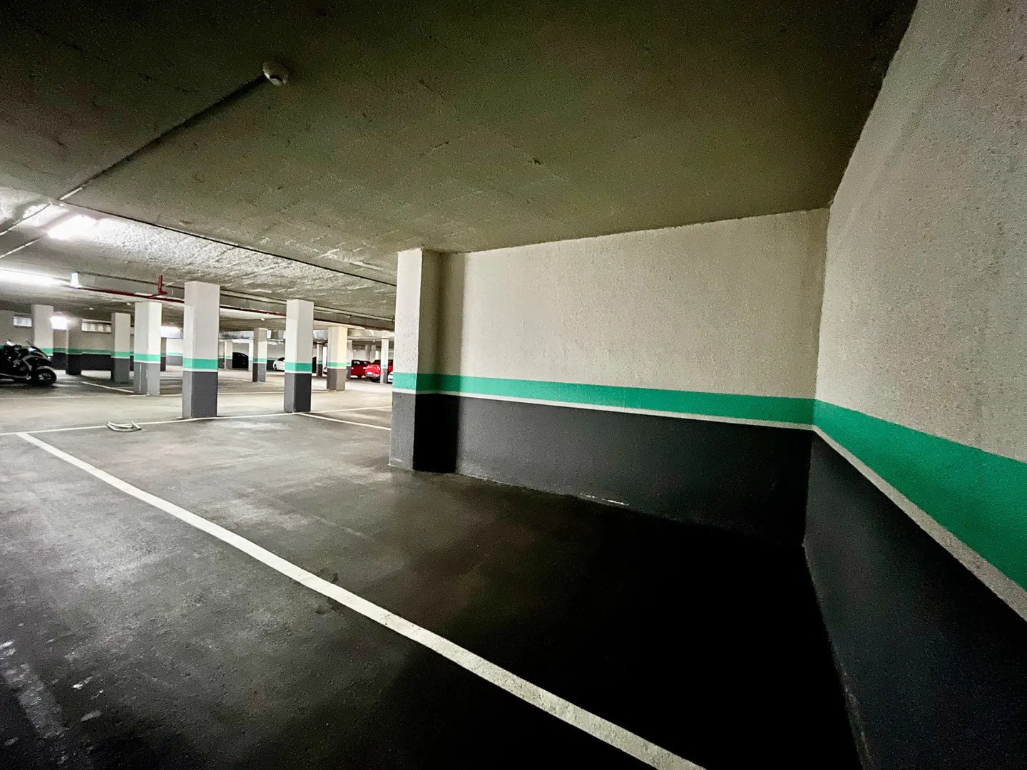 Indoor parking garage with white parking lines, gray floor, and white walls with a gray and green stripe.