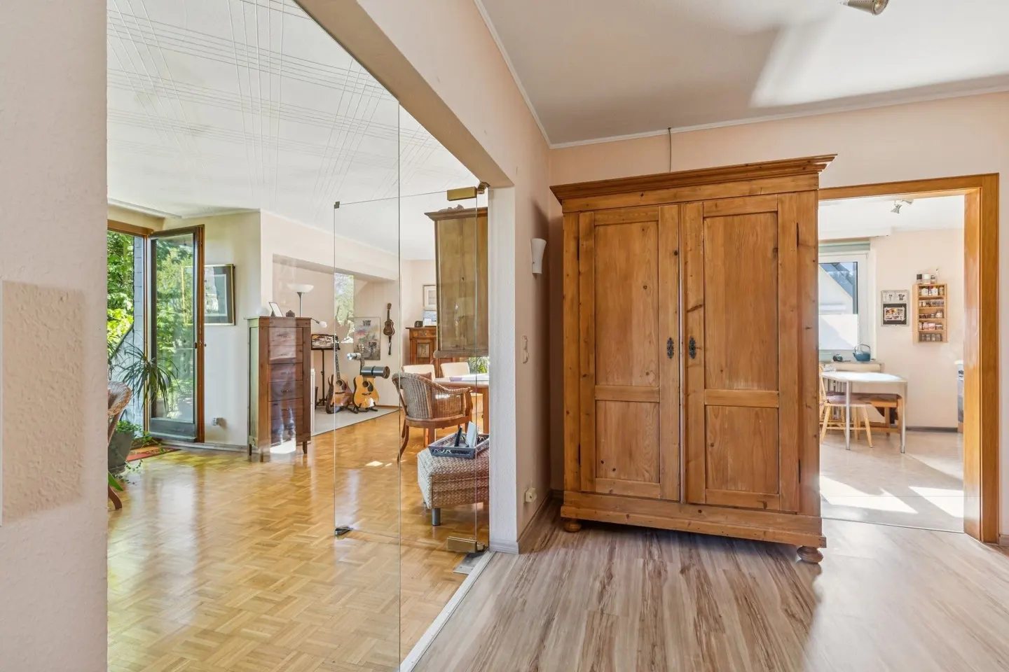 A view of a home's interior with a large wooden wardrobe, glass wall, and glimpses of a living room and kitchen.