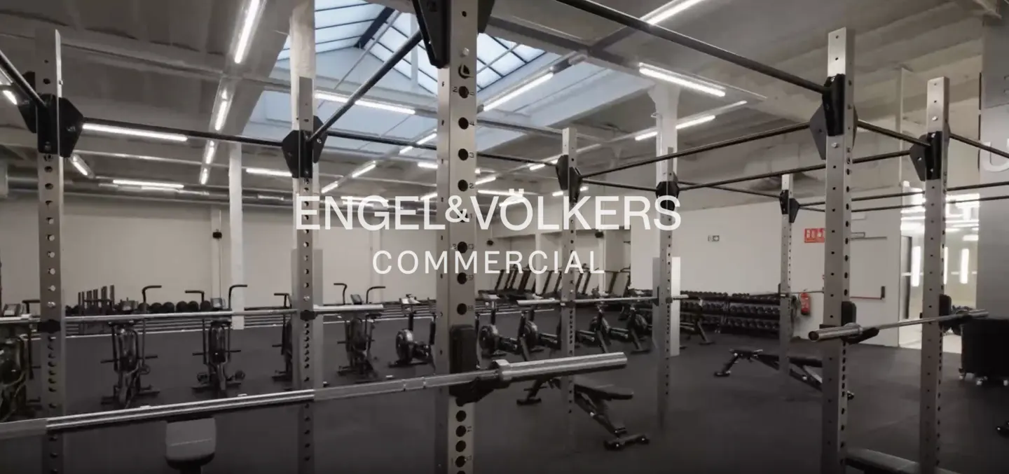 Gym interior with weight racks, exercise bikes, and dumbbells. Engel & Volkers Commercial logo overlay.