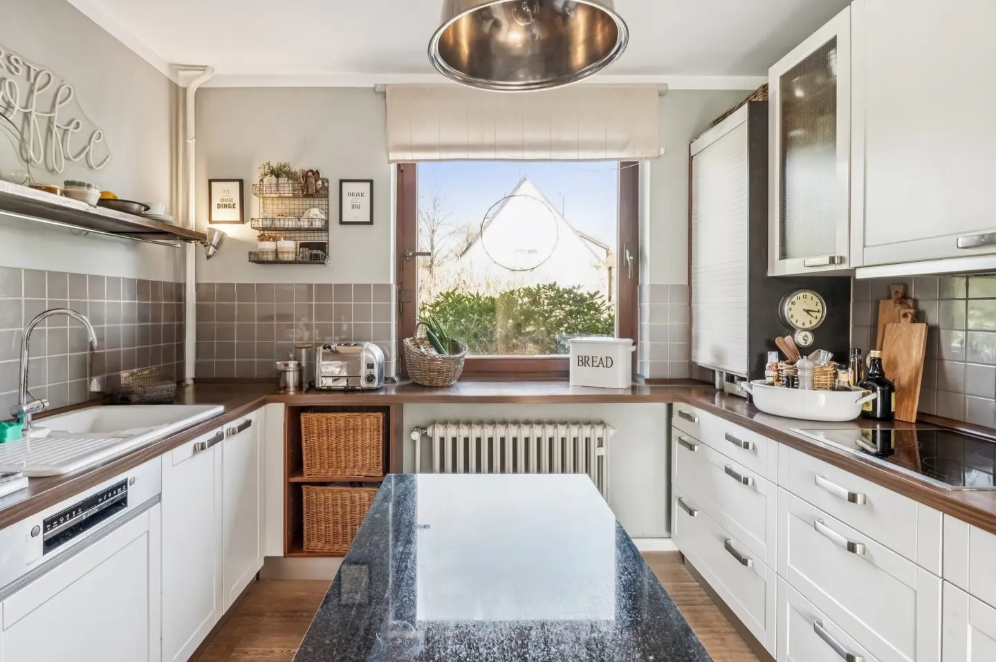 Bright kitchen with white cabinets, dark countertops, and a central island. A window overlooks a garden.