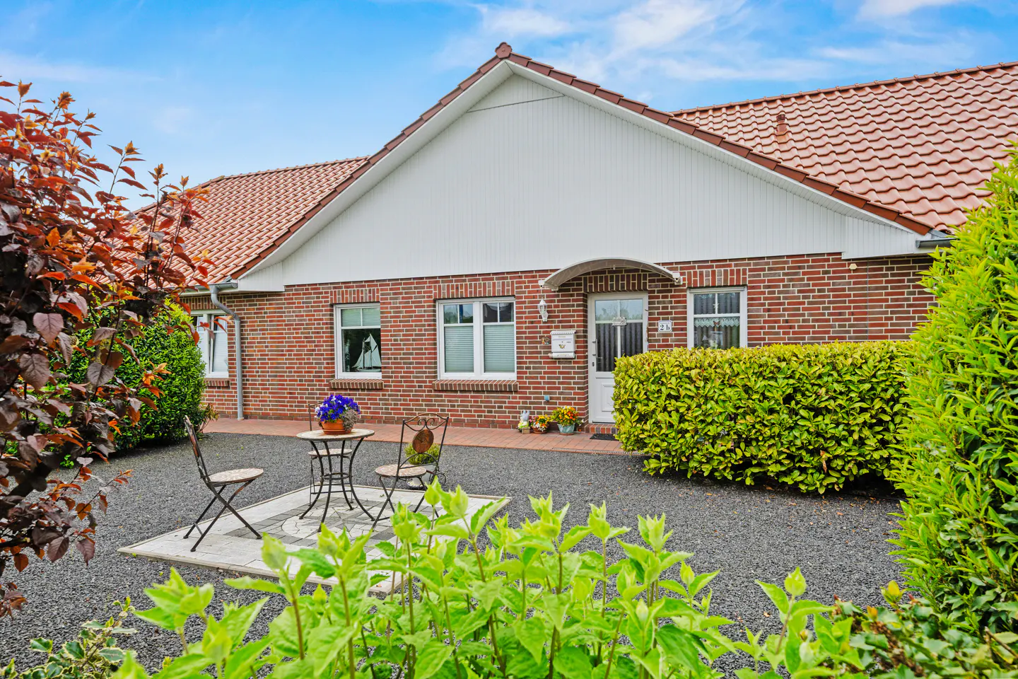 Exterior of a red brick house with a red tile roof and white trim. A table and chairs sit on a stone patio.