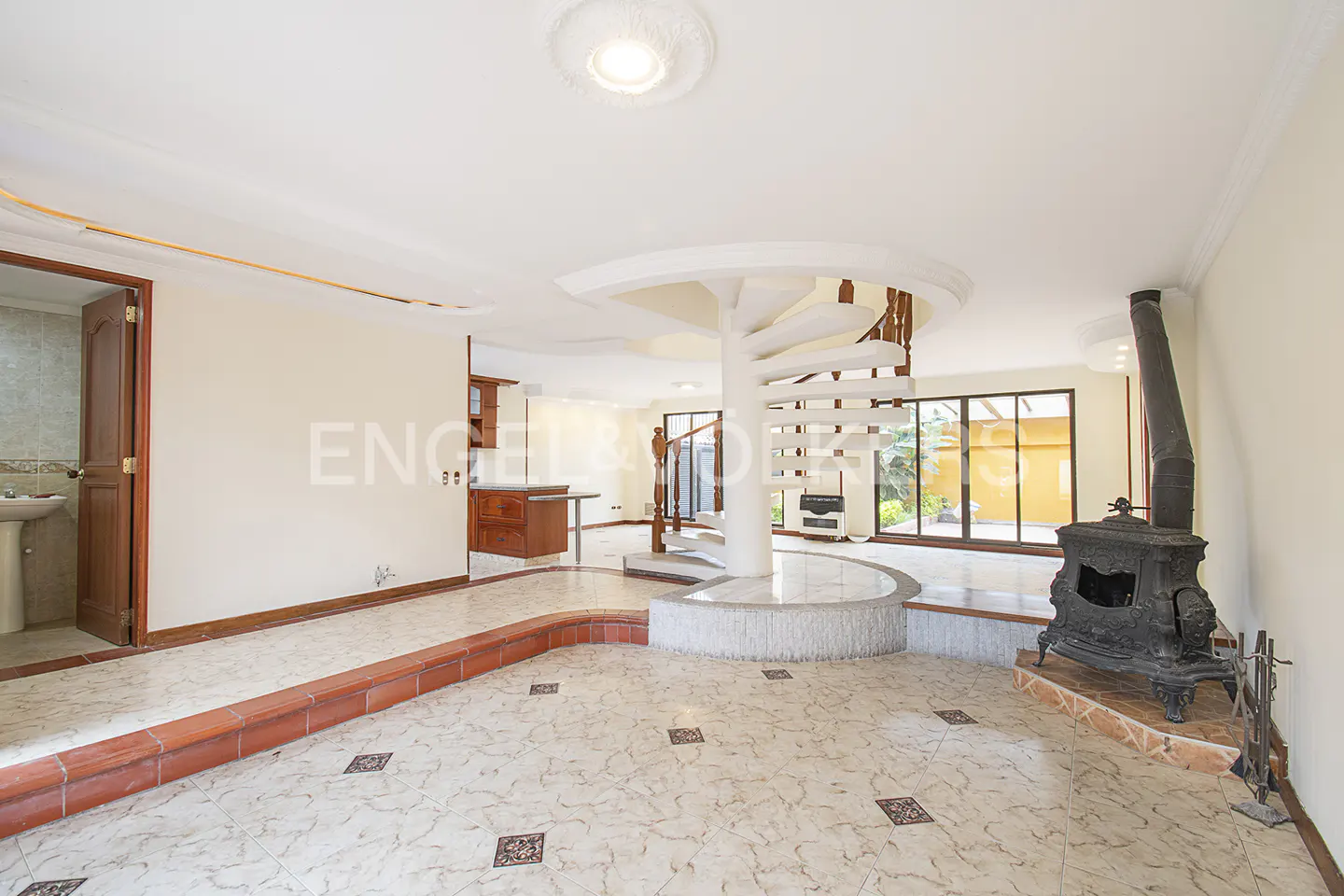 Bright living room with a spiral staircase, a black wood-burning stove, and marble tile flooring.