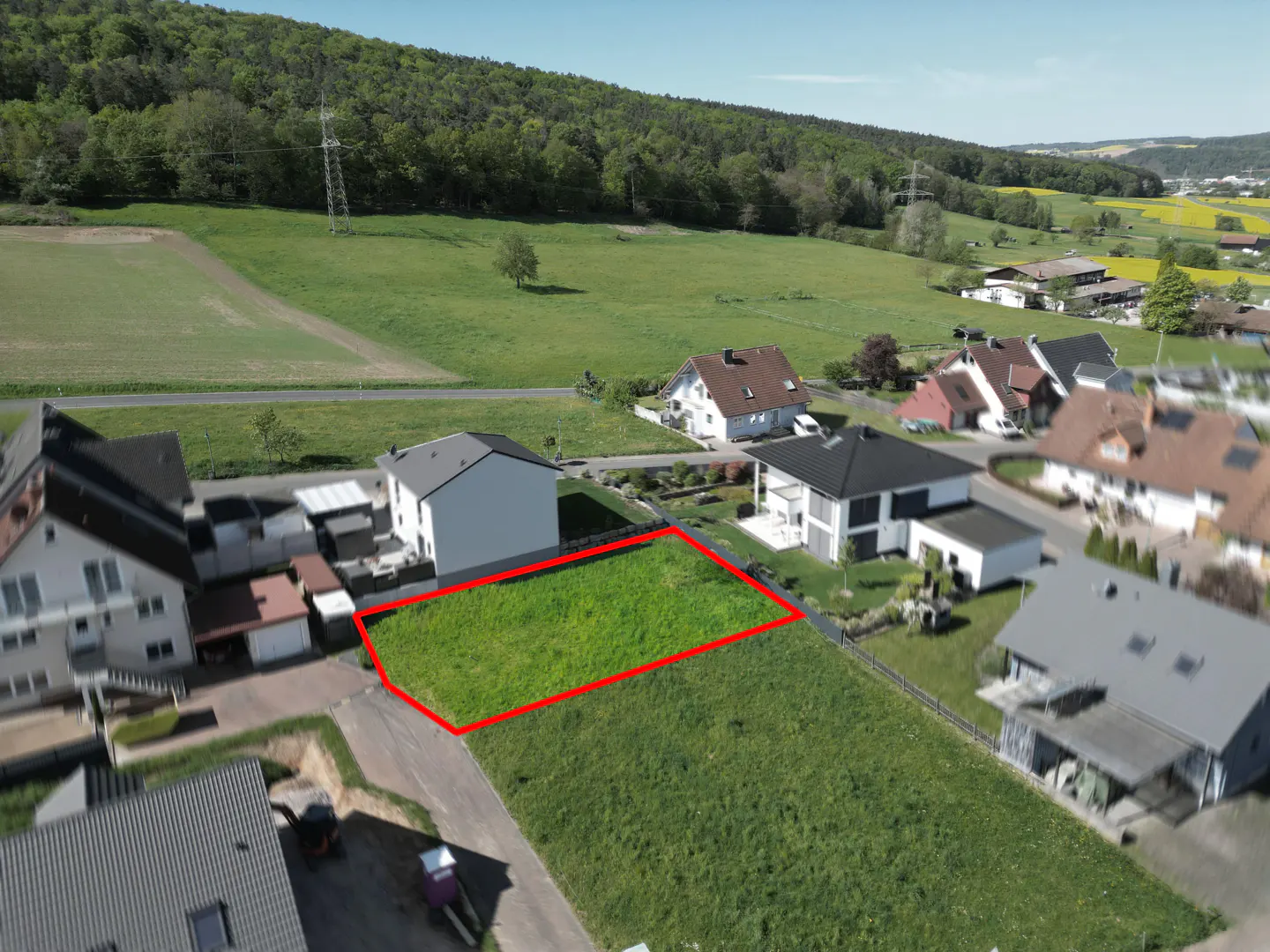 Aerial view of a grassy lot outlined in red, surrounded by houses and green fields.