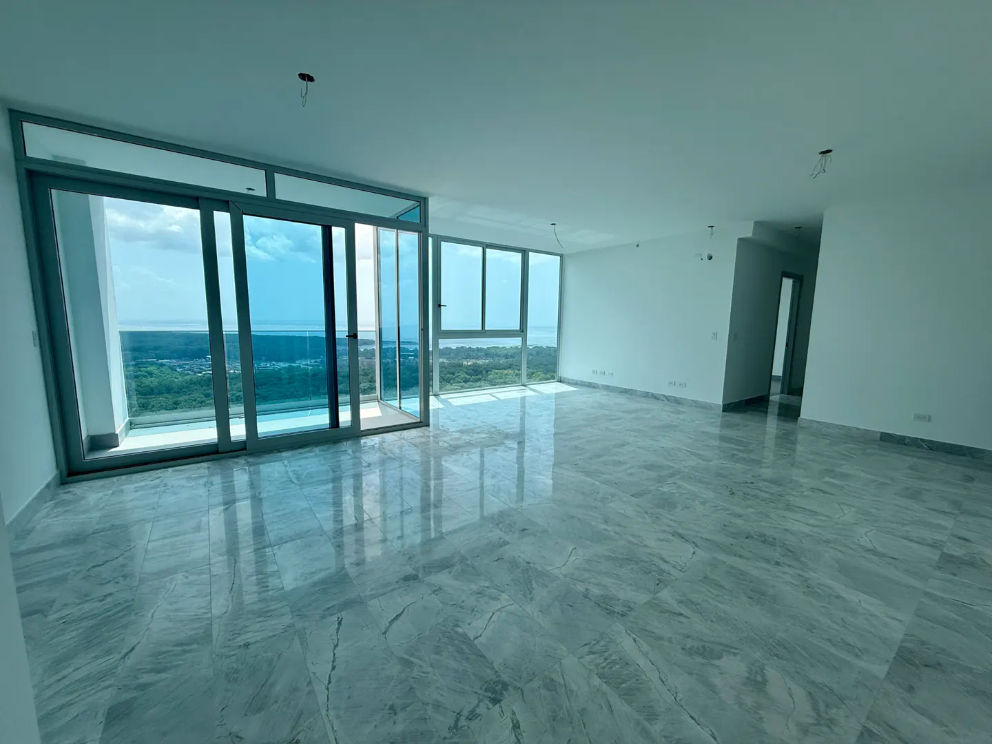 Unfurnished room with marble floors, white walls, and floor-to-ceiling windows. A view of the ocean and trees is visible through the windows.
