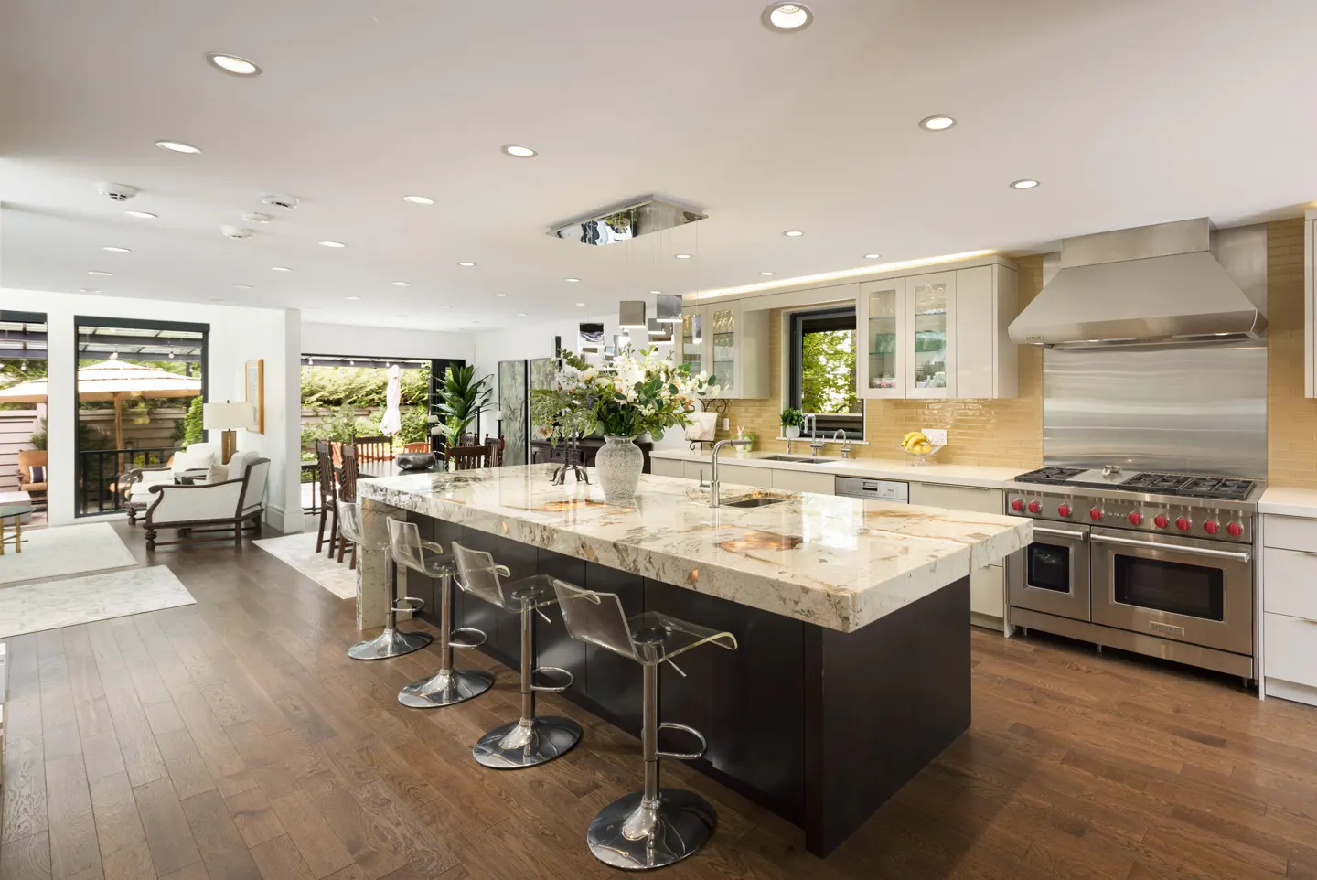 Open-concept kitchen with a marble island, clear stools, and stainless steel appliances. Hardwood floors and natural light.