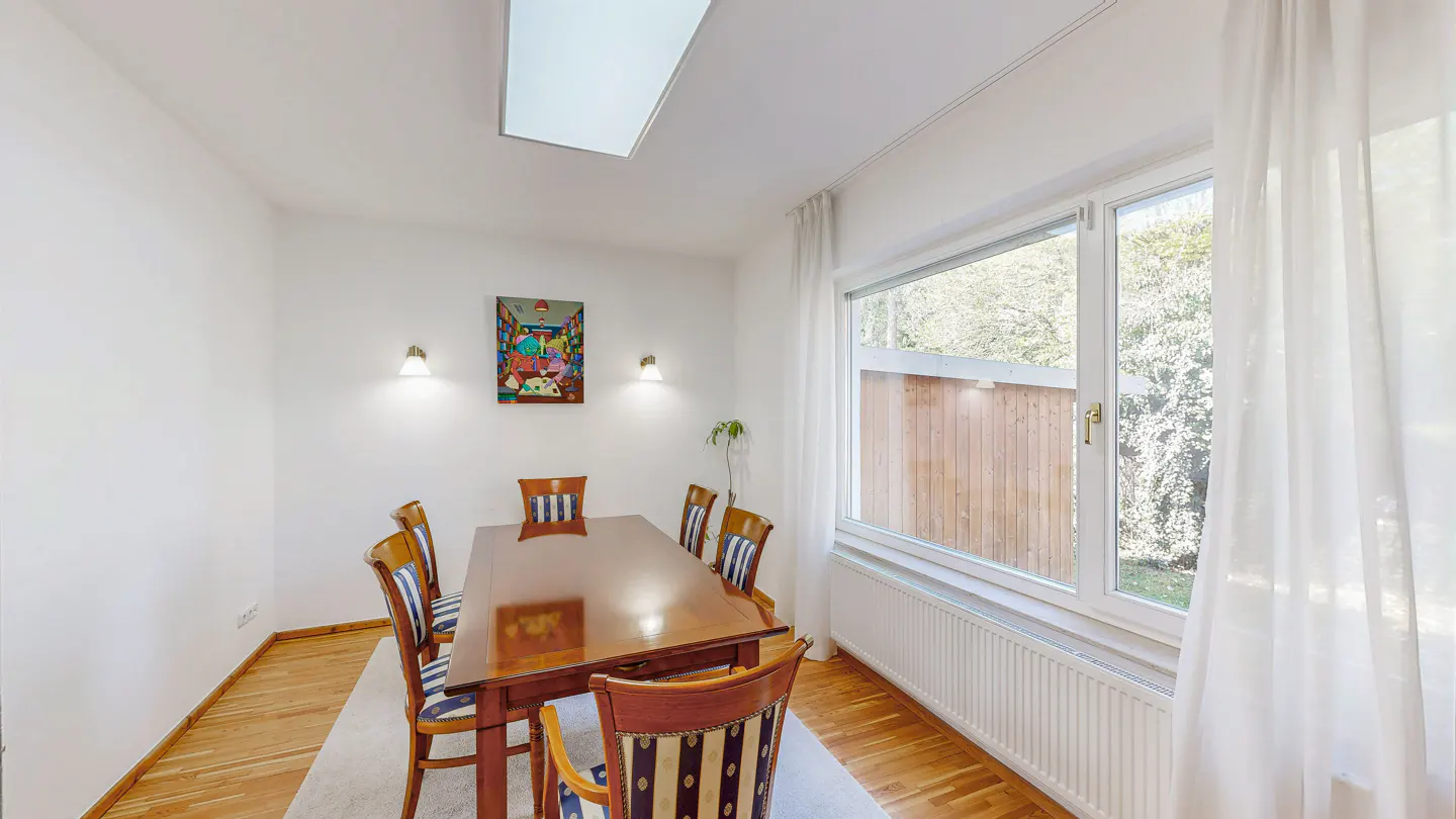 Bright dining room with a wood table, striped chairs, and white walls. A window with sheer curtains lets in natural light. Artwork hangs on the wall.