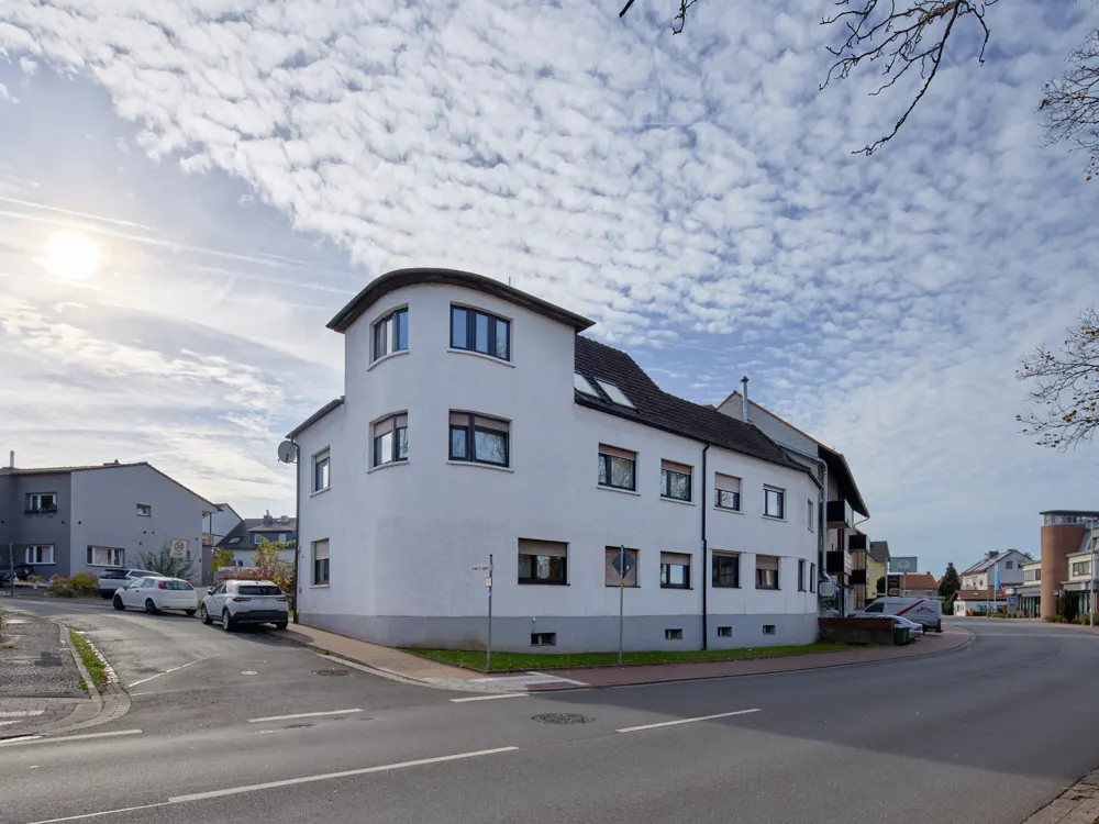 A three-story white building with black framed windows on a street corner under a cloudy sky.