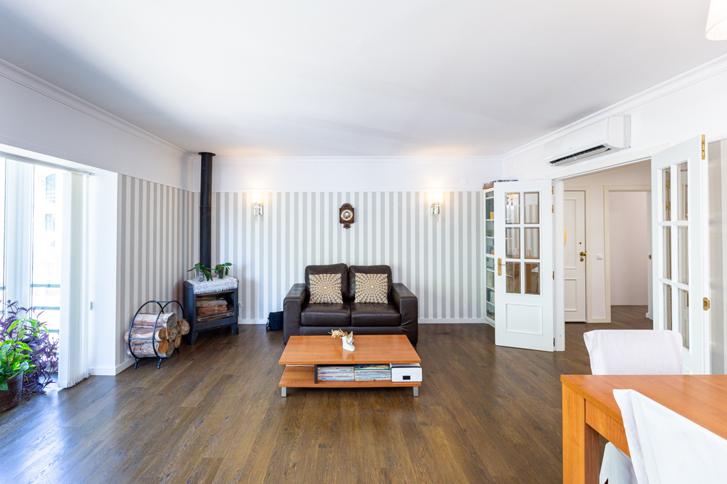 Living room with dark leather sofa, wooden coffee table, wood-burning stove, and striped wallpaper on hardwood floors. [AI-generated text]