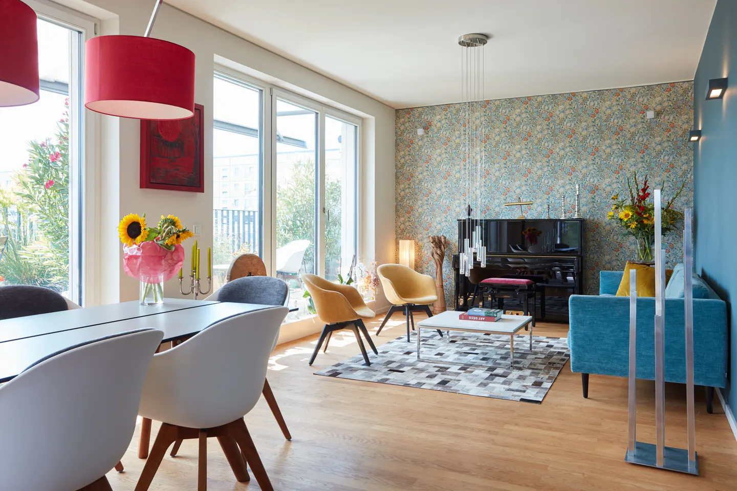 Bright living room with a dining table, white chairs, yellow armchairs, a blue sofa, and a black piano.