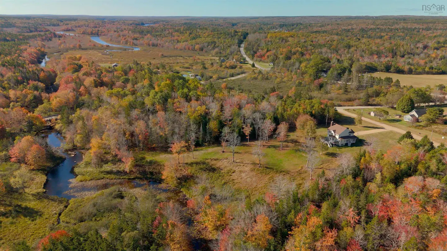 Aerial view of a white house surrounded by colorful autumn trees and a winding river.