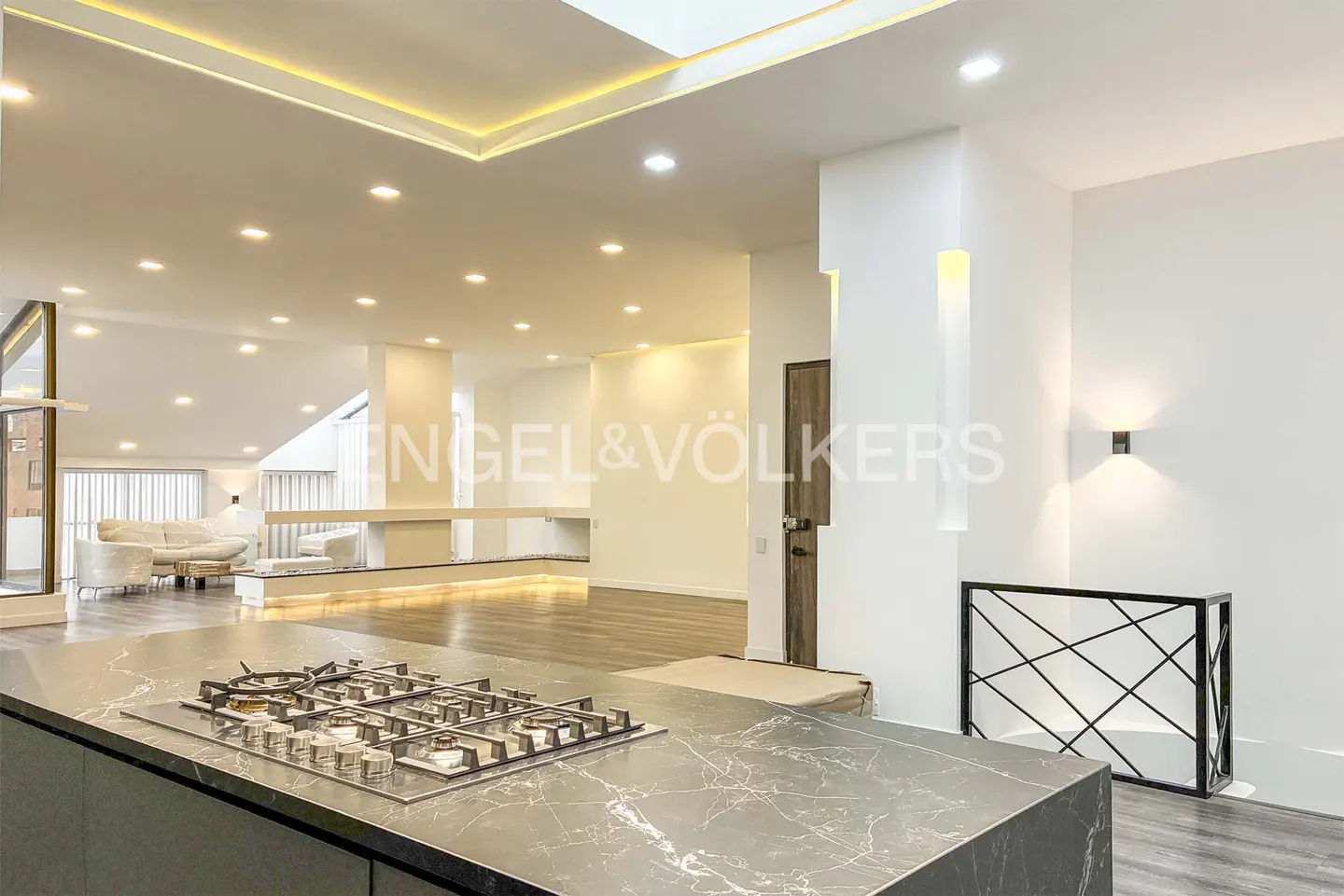 Open-concept kitchen and living room with white walls and recessed lighting. A black marble countertop island features a gas stovetop.