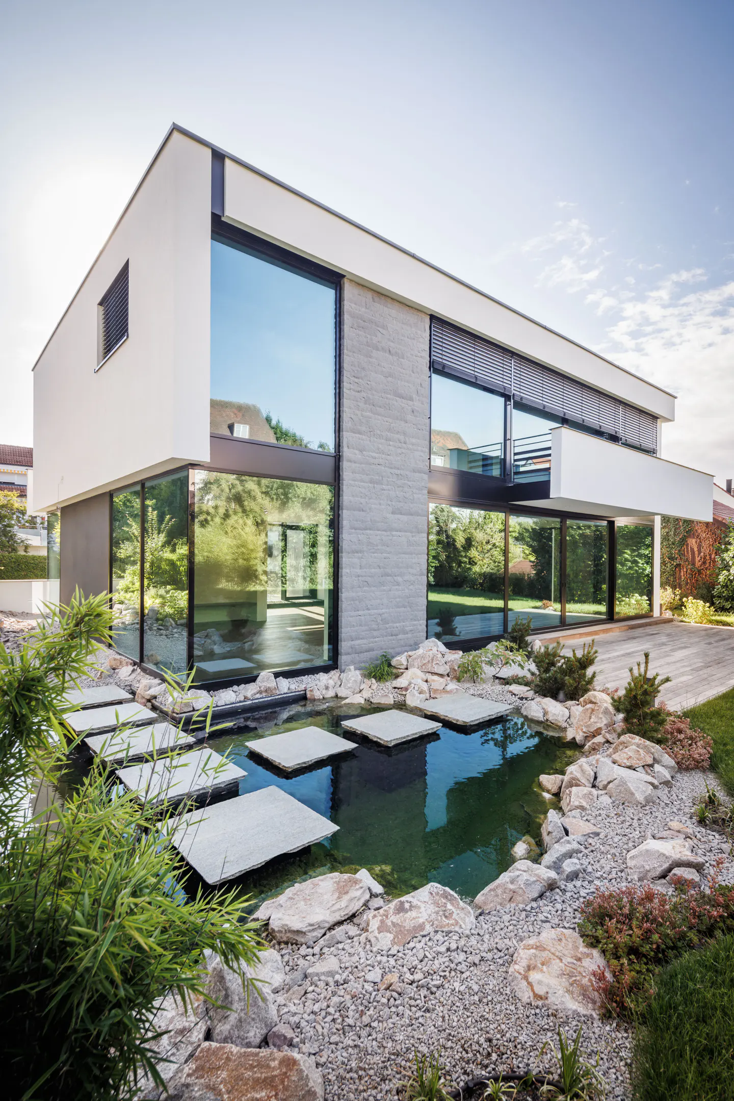 Modern two-story white house with large windows and a pond with stepping stones in the front yard.