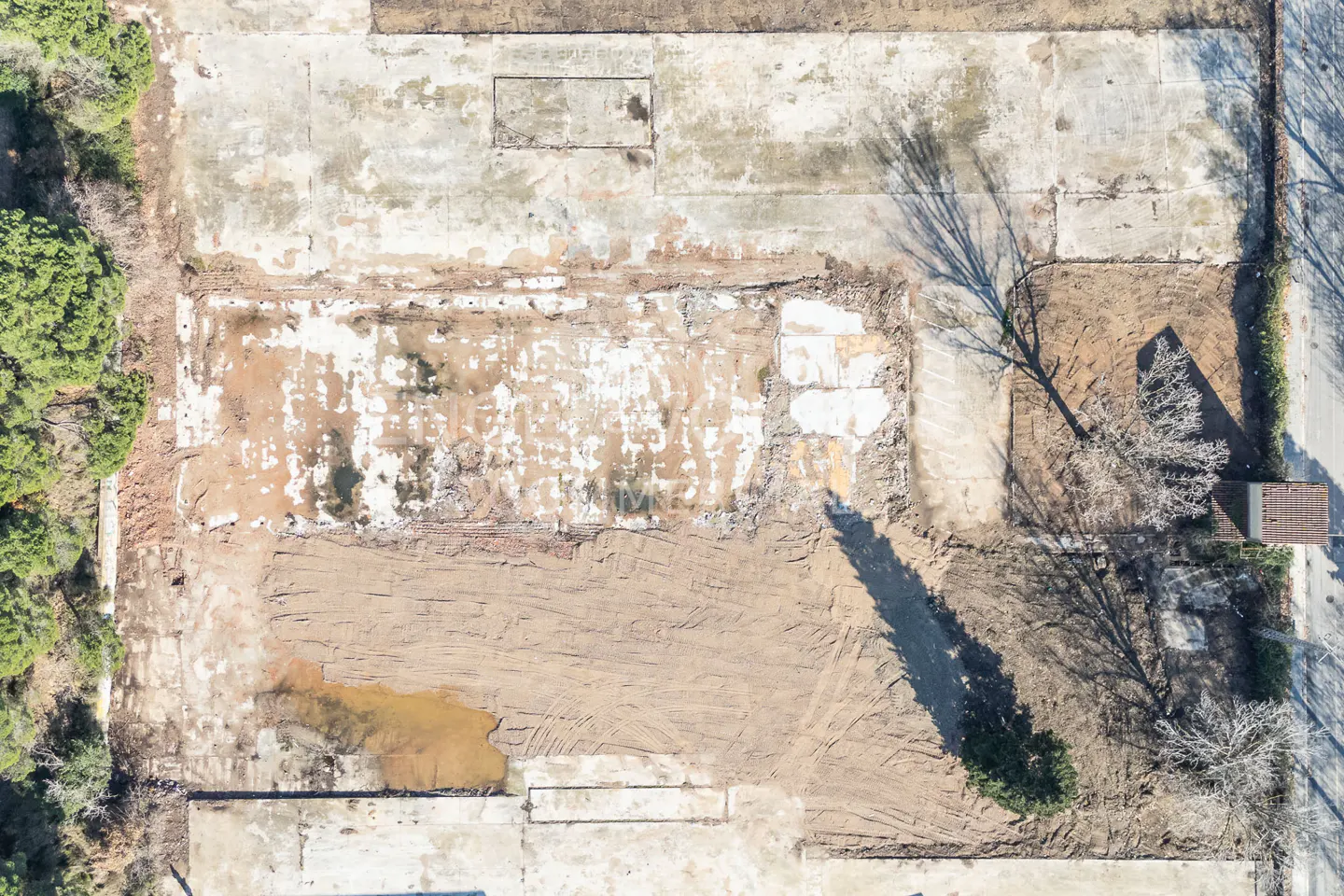 Aerial view of a vacant lot with concrete pads, dirt, and some trees.