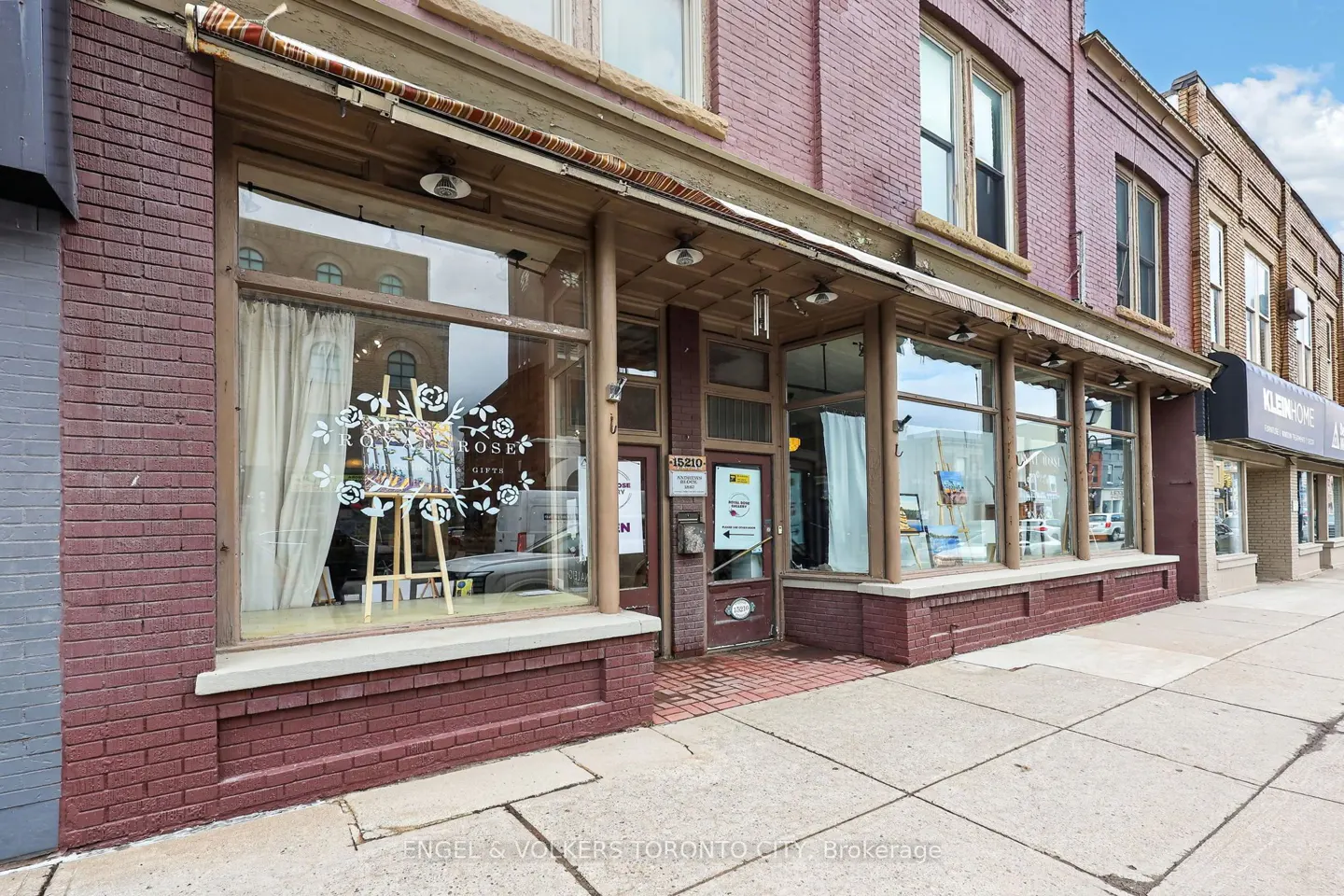 Exterior of a brick building with large windows displaying art and gifts. A sidewalk runs in front.