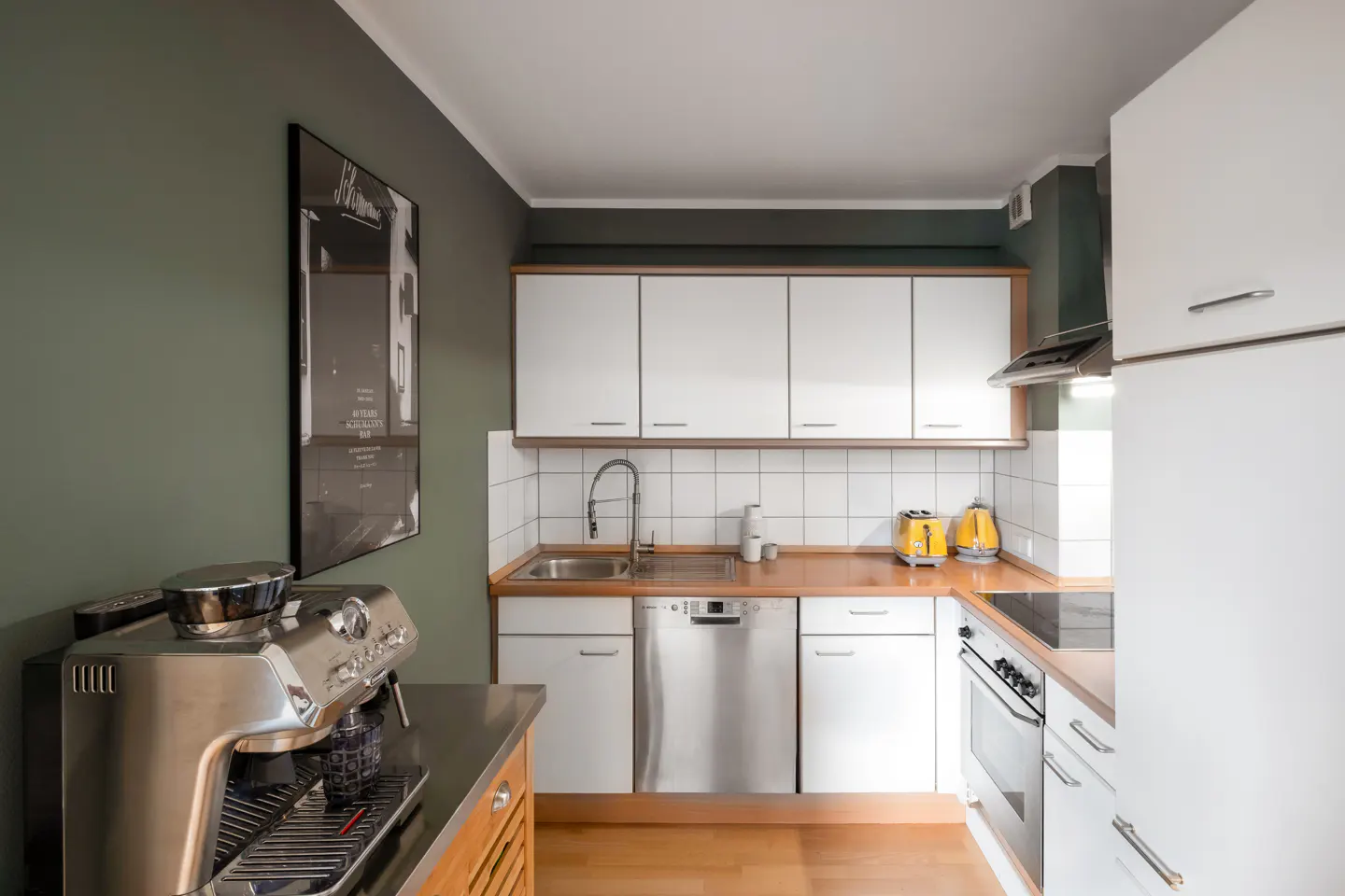 Modern kitchen with white cabinets, wood countertops, stainless steel appliances, and sage green walls.