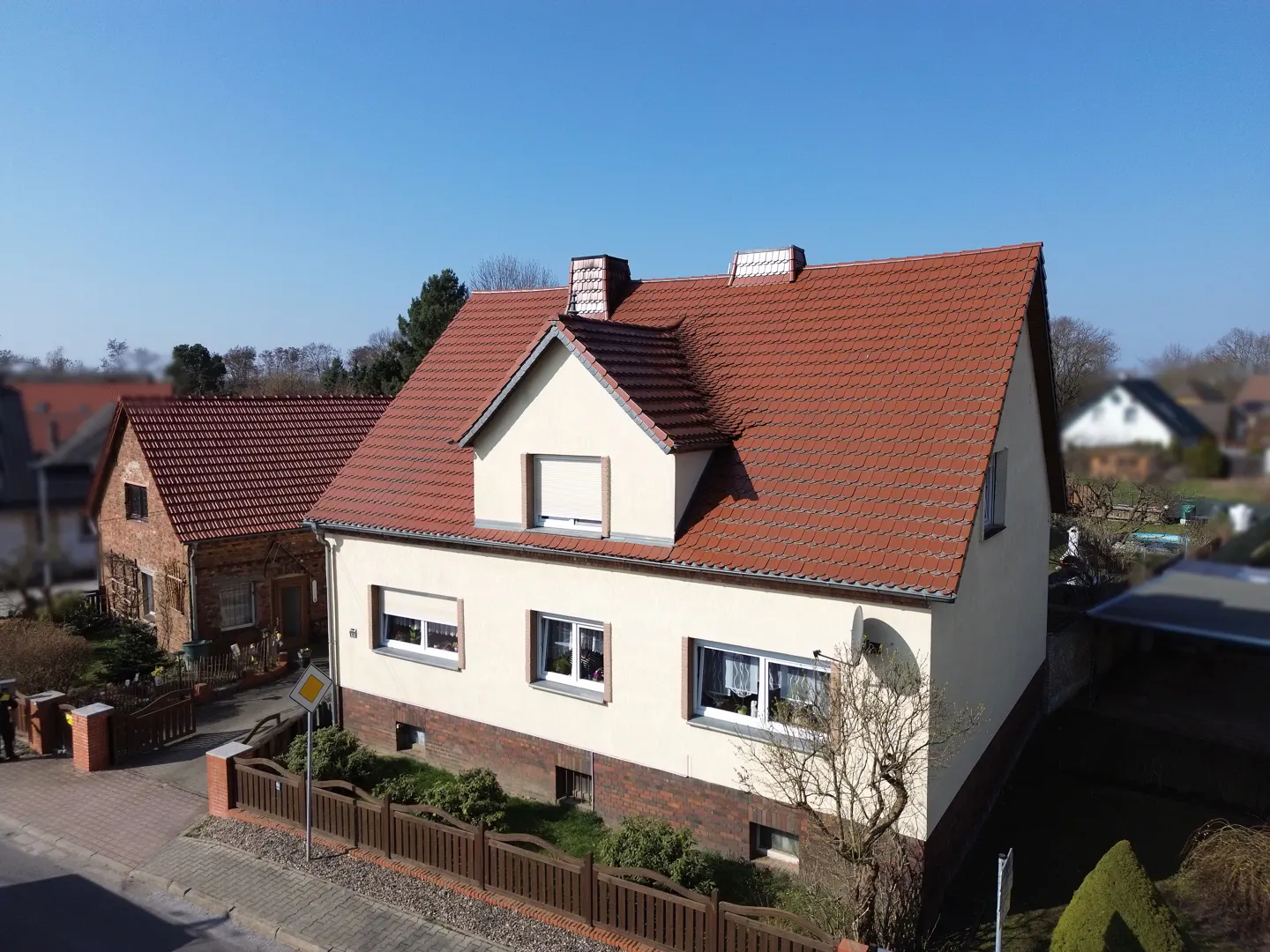Two-story house with a red tile roof and cream-colored siding, viewed from above on a sunny day.