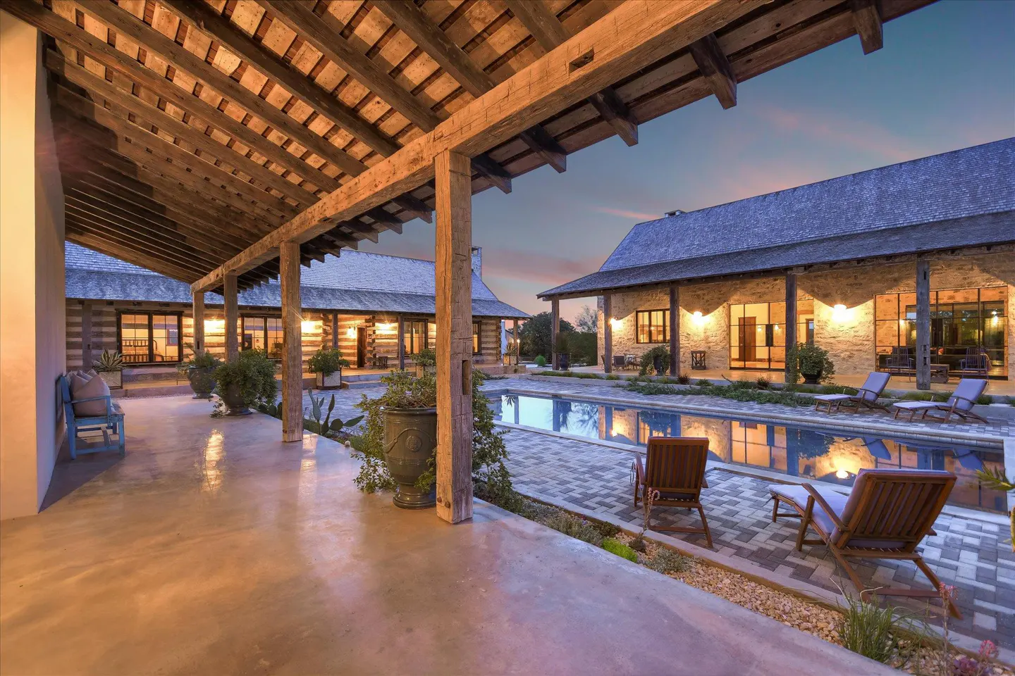 Exterior view of a luxury home with a pool, lounge chairs, and a covered patio with wooden beams.