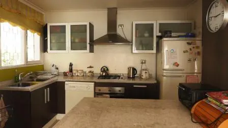 A bright kitchen with white cabinets, stainless steel appliances, and a tan island. A window with yellow curtains is on the left.