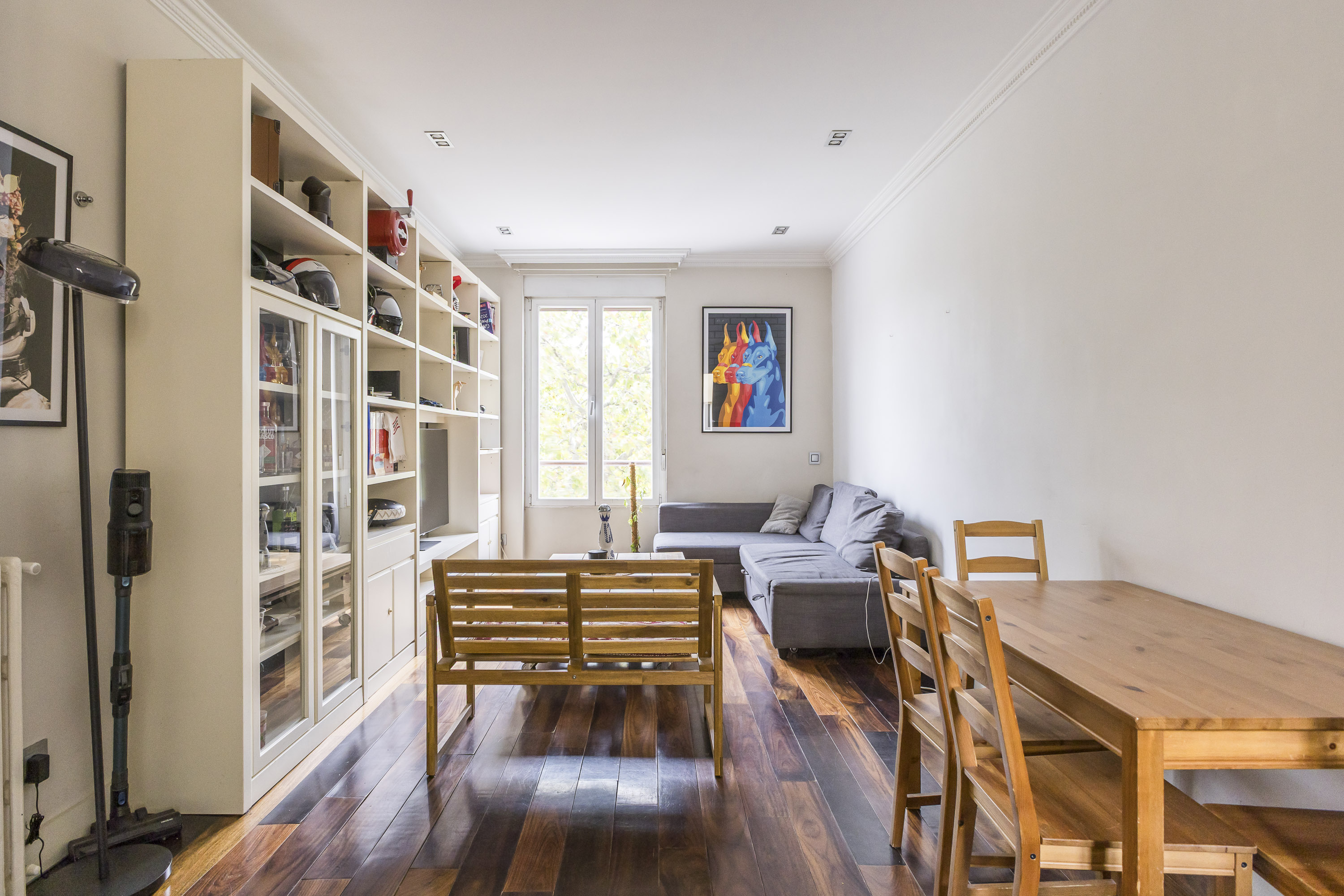 Living room with hardwood floors, a wooden bench, grey sectional sofa, dining table, and large white built-in shelving unit. [AI-generated text]