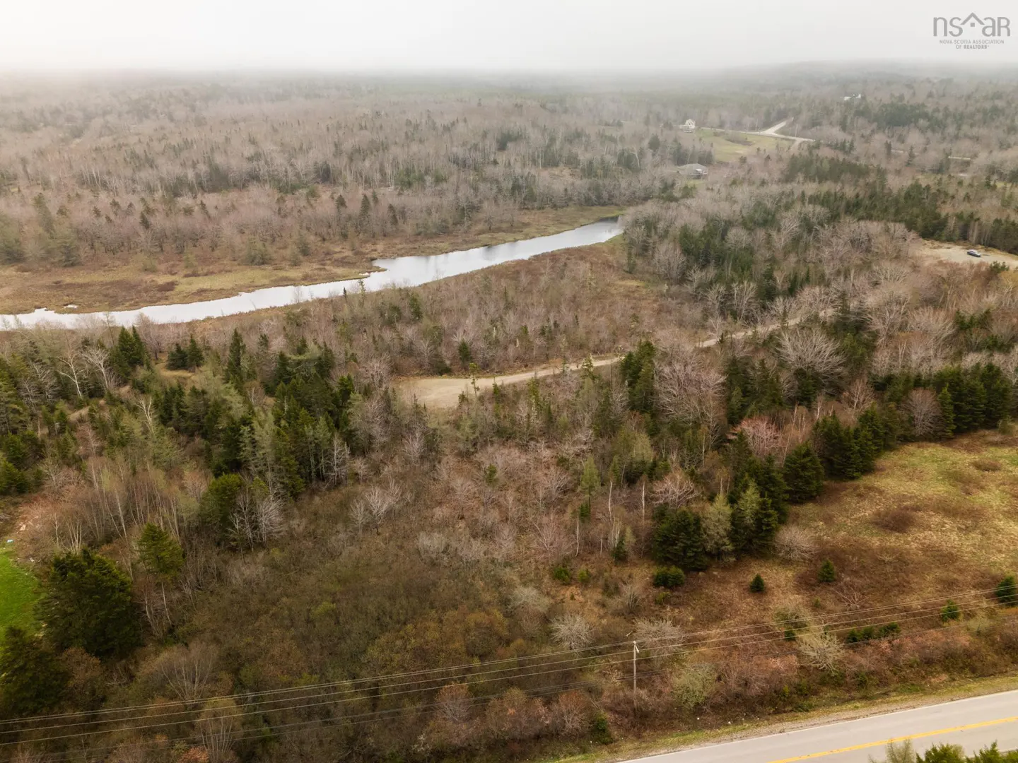 Aerial view of wooded land with a river running through it, next to a road.