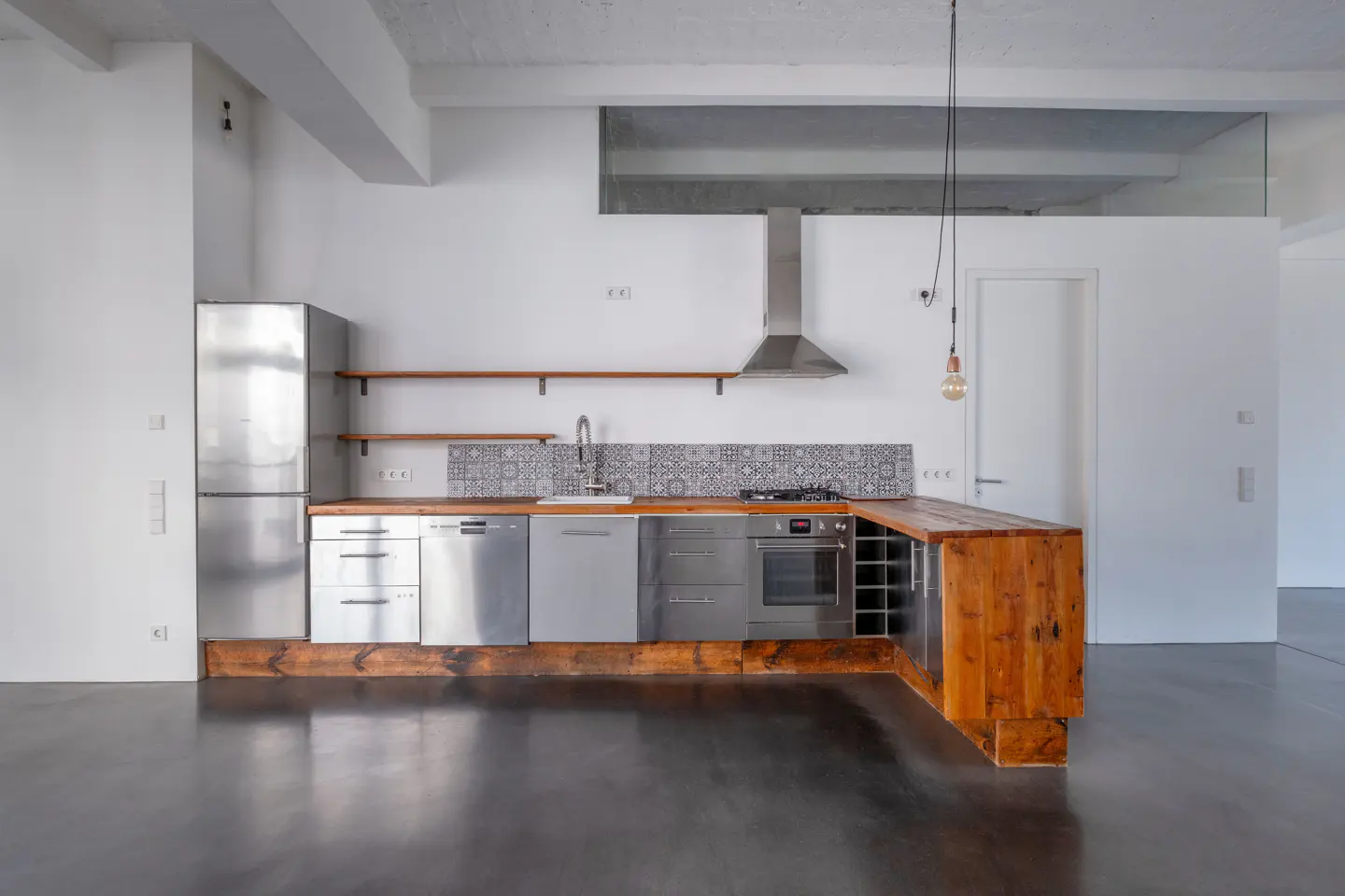 Bright, modern kitchen with stainless steel appliances, wood countertops, and patterned backsplash. A stainless steel range hood is above the stove.