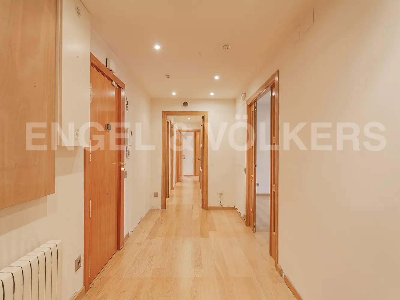 Bright hallway with light wood flooring, beige walls, and multiple wooden doors leading to other rooms.