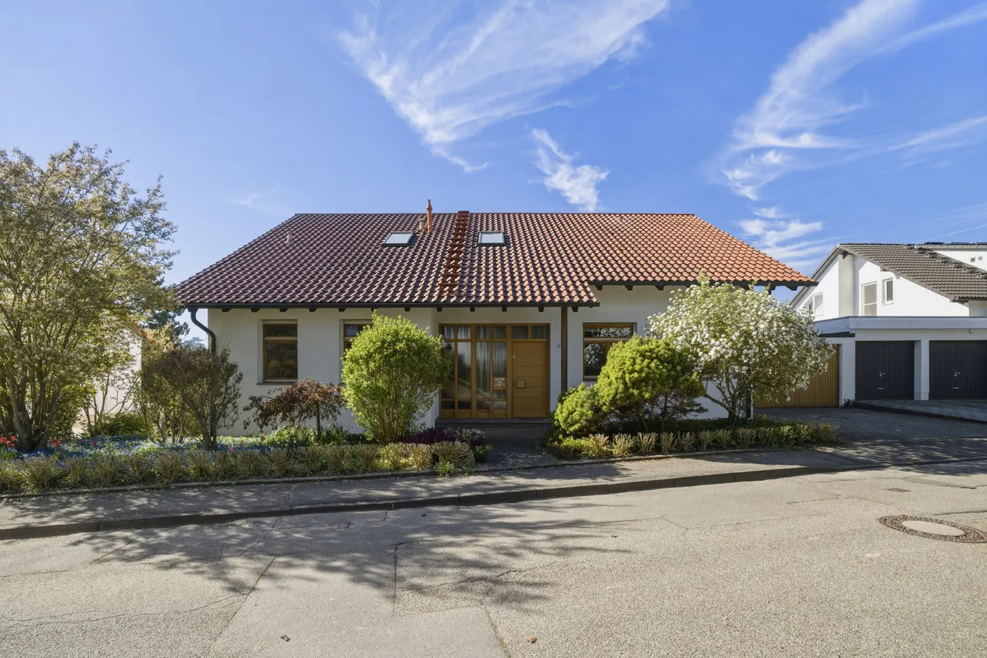Front view of a one-story white house with a red tile roof, green bushes, and a blue sky.