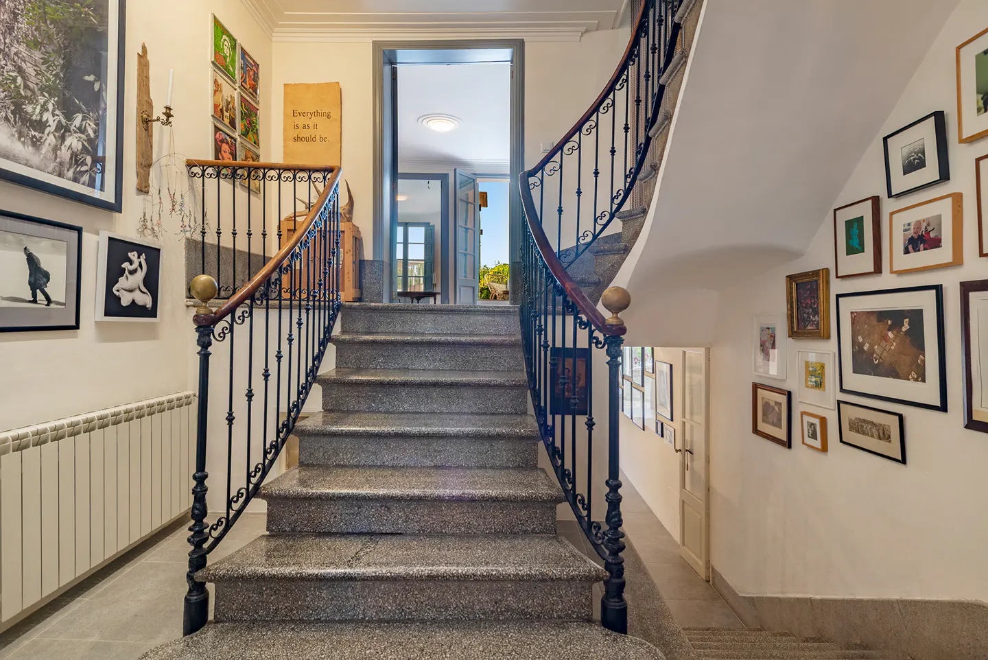 Interior view of a staircase with granite steps, black wrought iron railing, and walls adorned with framed art.