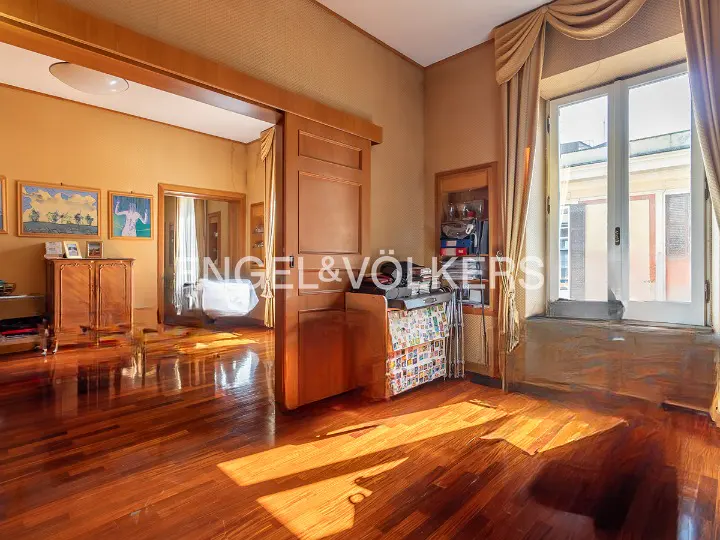 Interior view of a room with hardwood floors, a large window with curtains, and a doorway to another room.