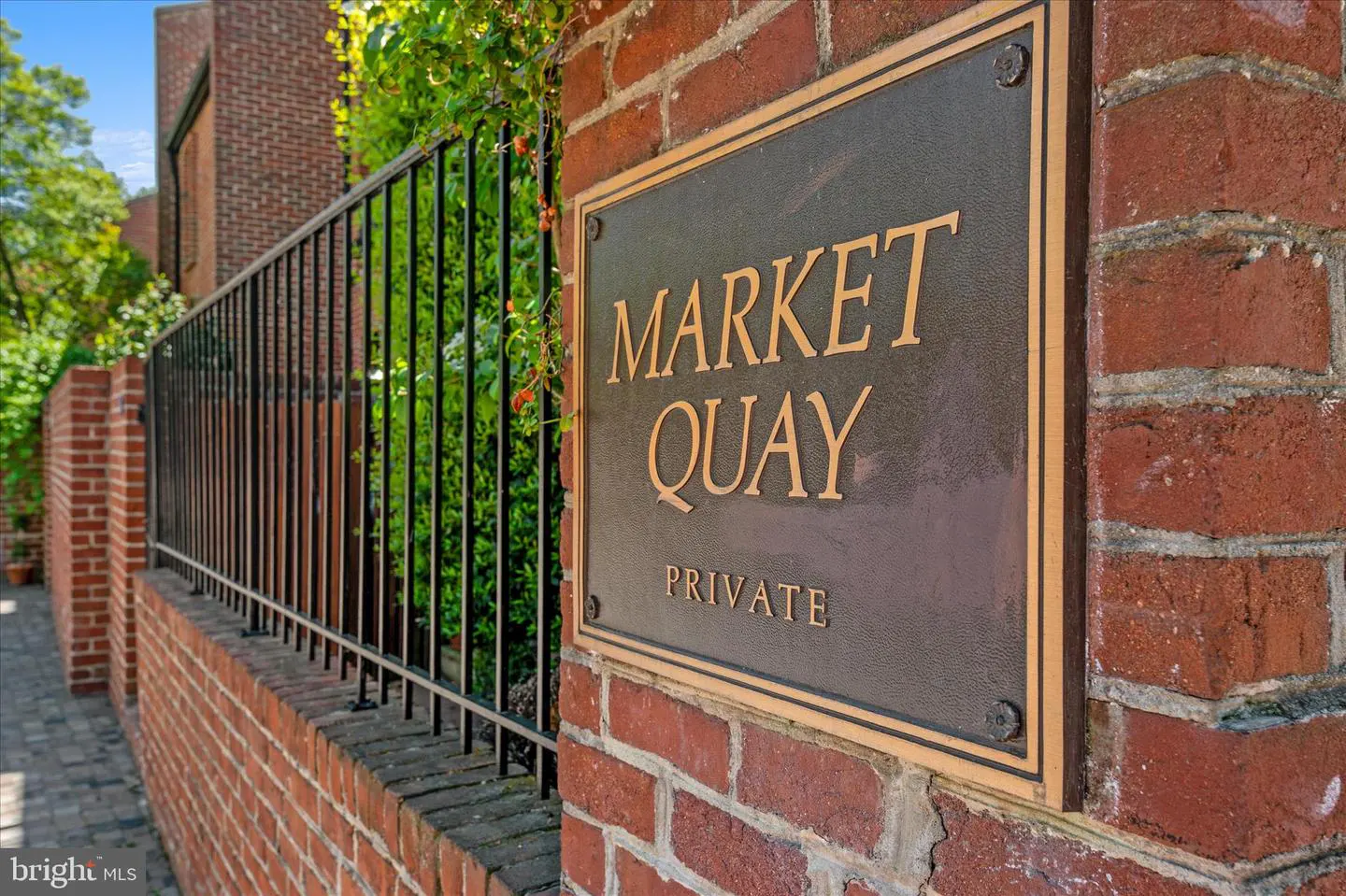 Brick wall with a black metal fence and a bronze sign that reads "Market Quay Private".