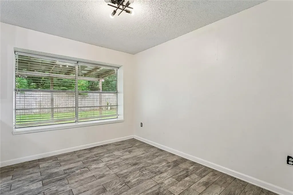 Empty room with white walls, gray wood-look tile floor, and a window with blinds overlooking a green yard. A modern light fixture is on the ceiling.