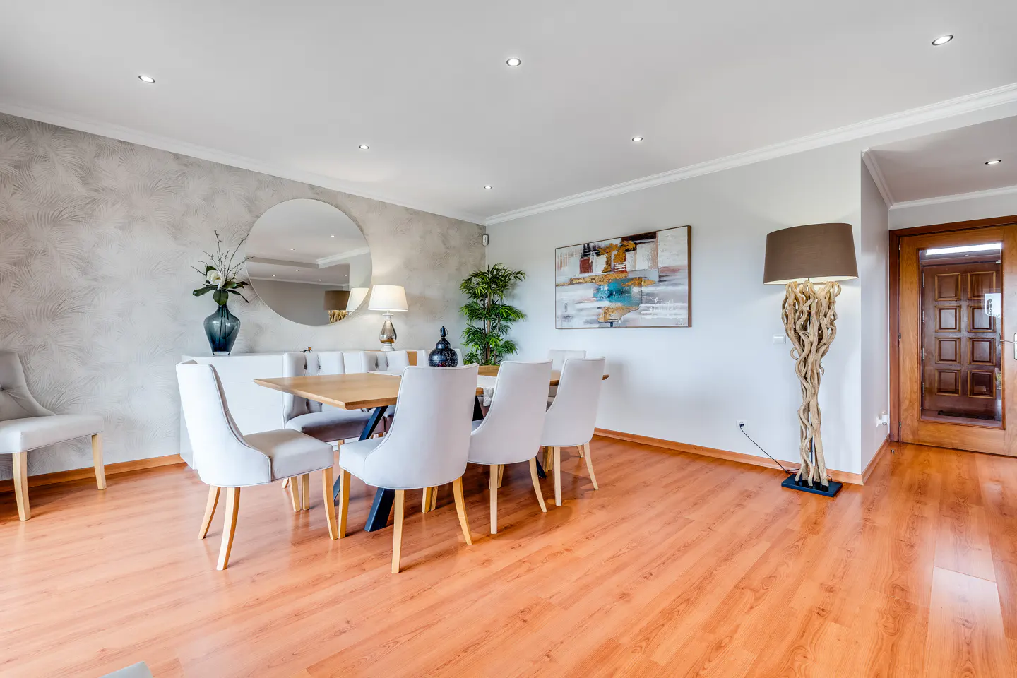 Bright dining room with wood floors, a table with six white chairs, and a driftwood floor lamp near a wooden door.