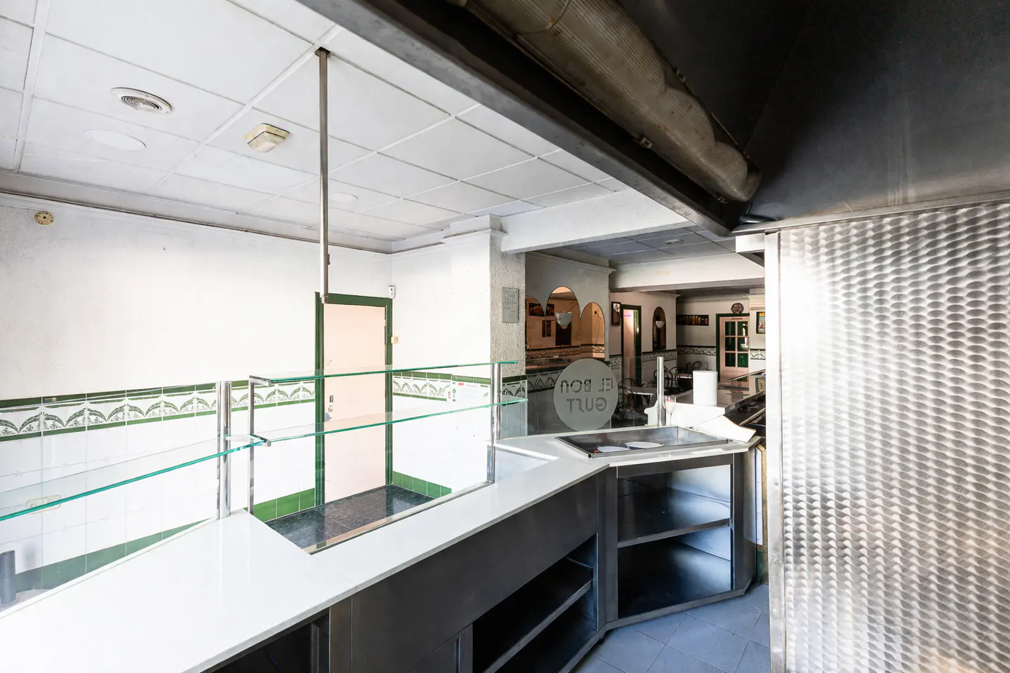 Interior view of a commercial kitchen with white walls, stainless steel counters, and glass display cases.
