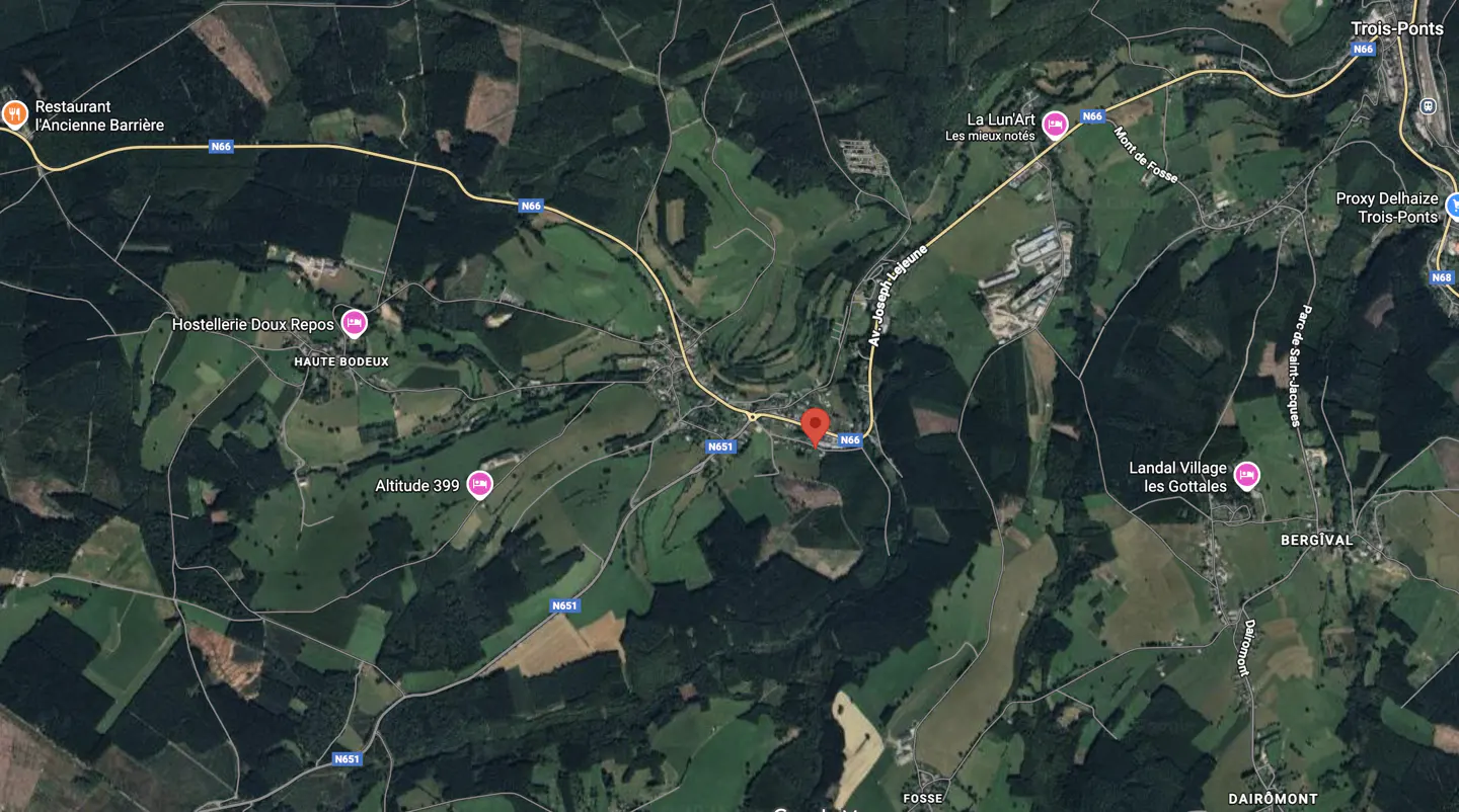 Aerial view of a rural area with green fields, forests, and roads, with a red pin marking a location.