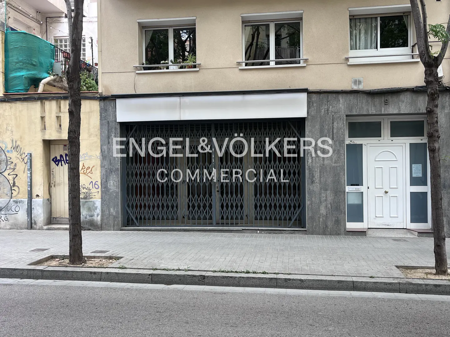 Exterior of an Engel & Völkers Commercial office with a closed metal gate. The building is beige with gray accents and white trim.